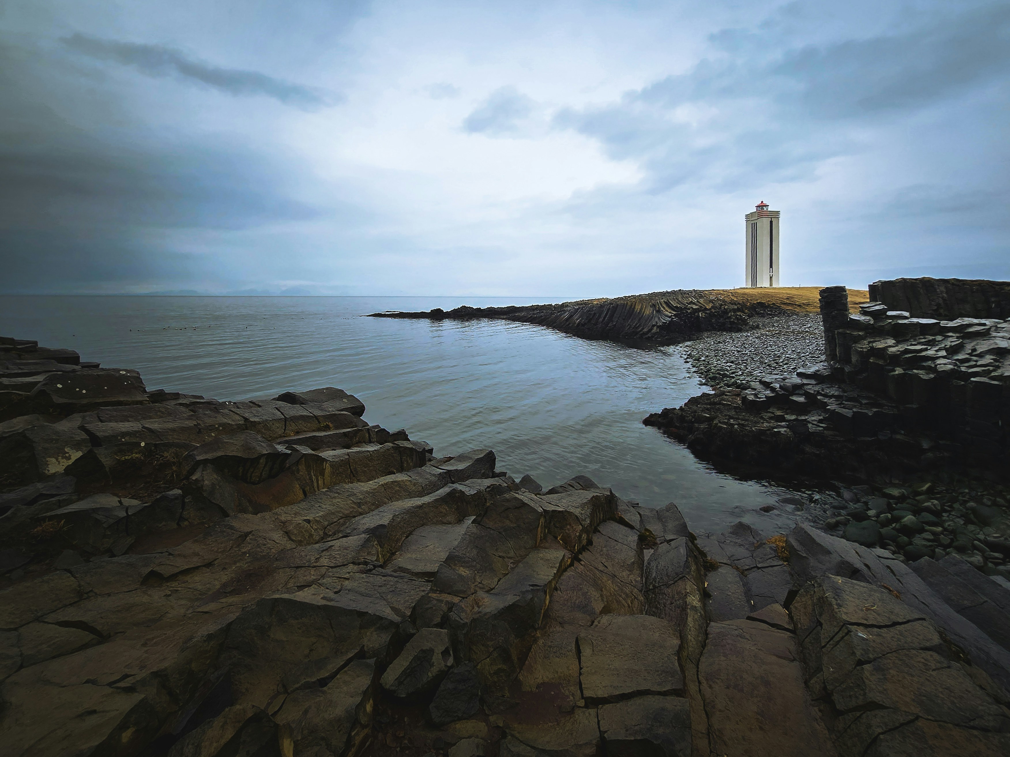 A lighthouse stands beside the calm sea.