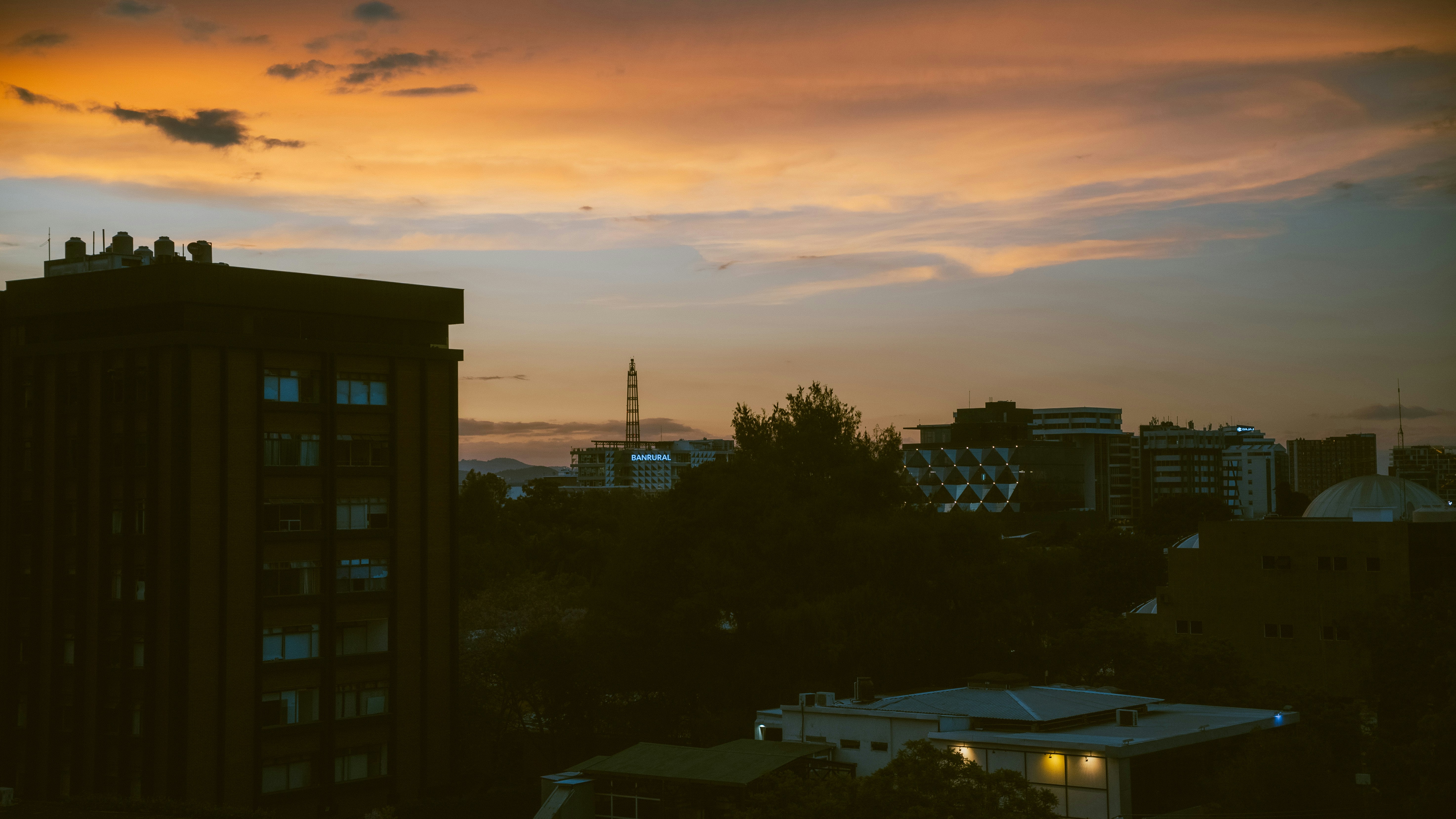Buildings are silhouetted against a colorful sunset sky.