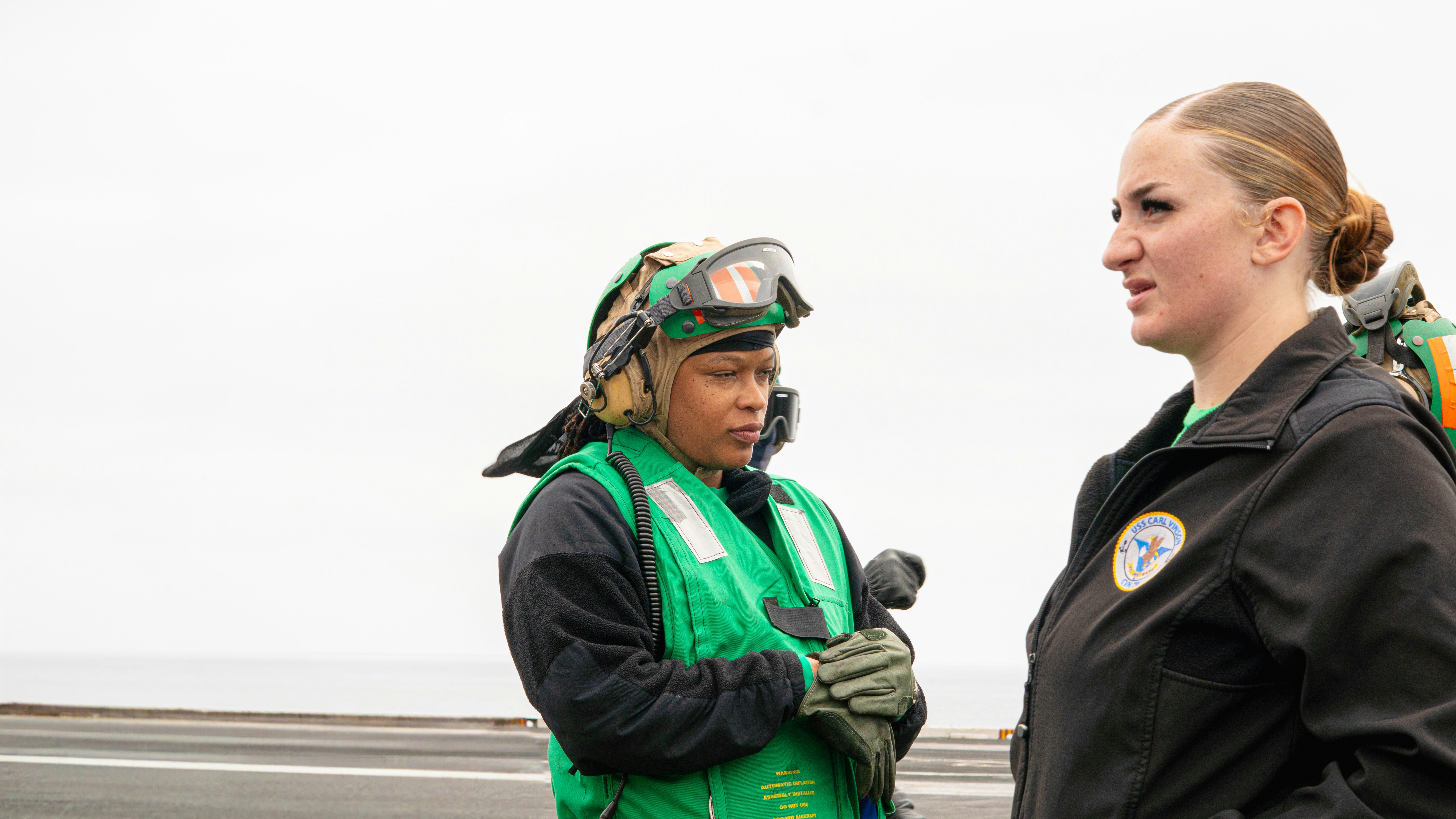 Two navy officers converse on a flight deck.
