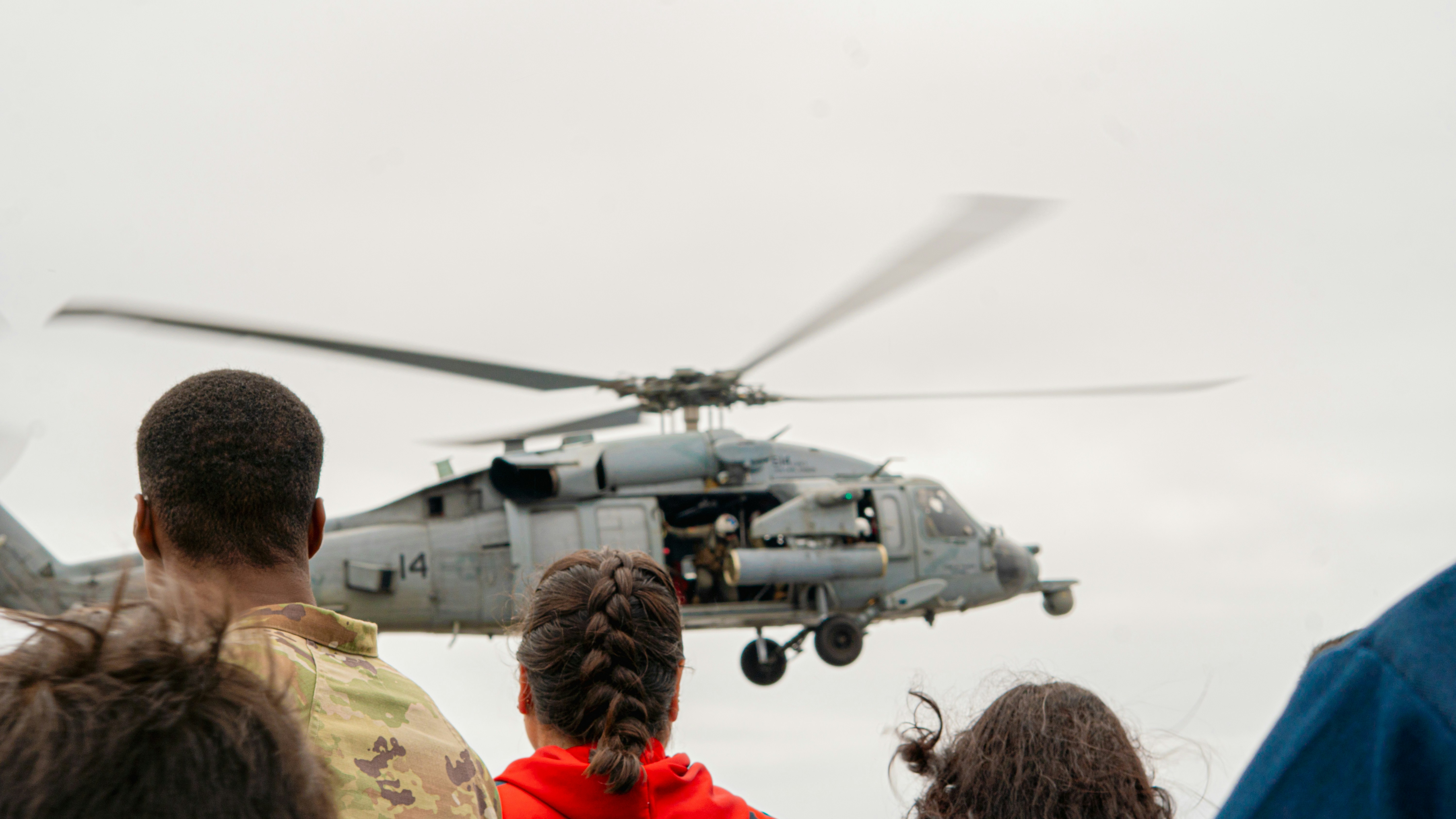 People watch a helicopter taking off.