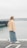 A woman stands by the water, looking out.