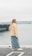 A woman stands by the water, looking out.