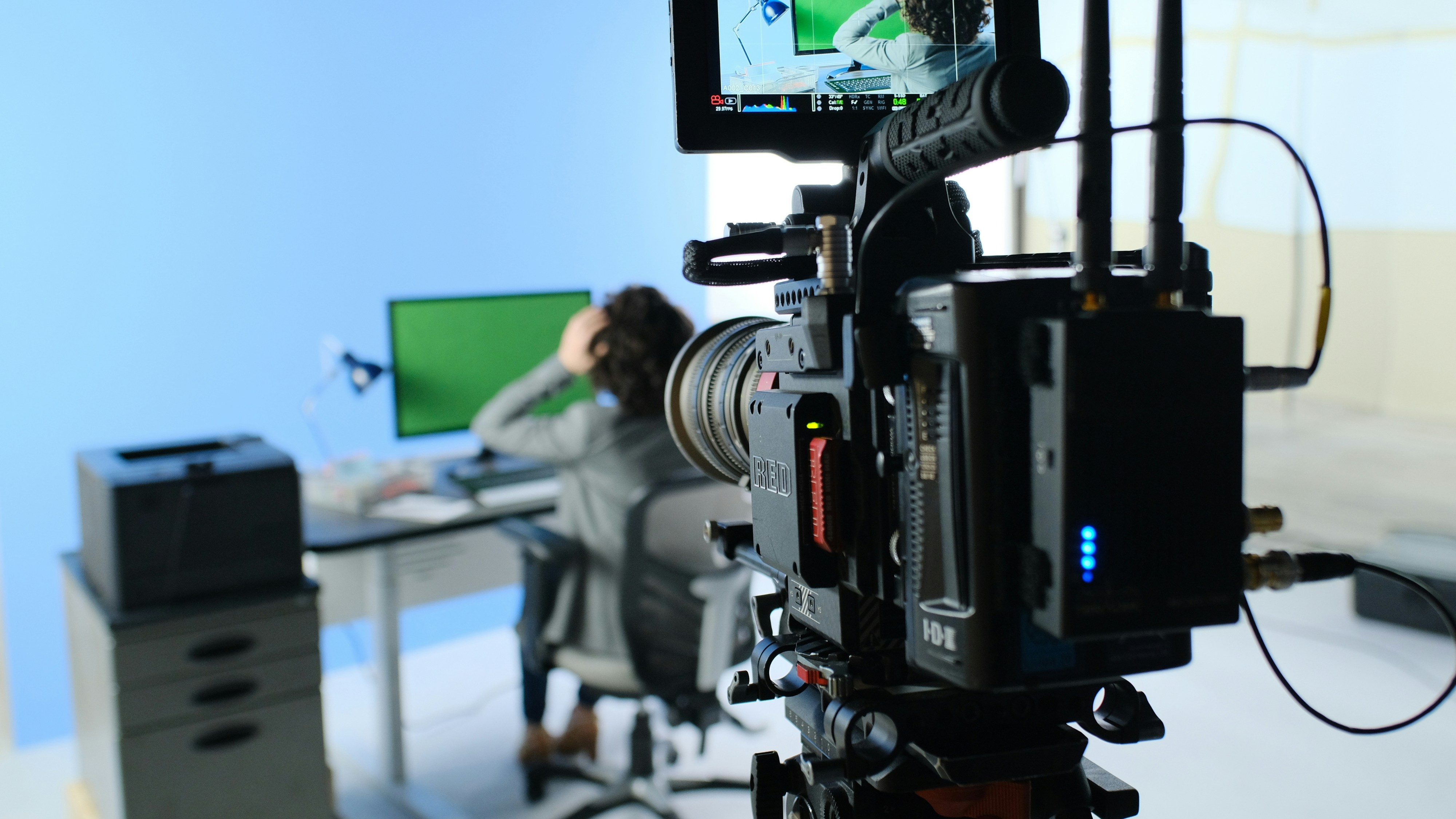 A camera filming a person in front of a screen.