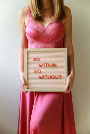 Woman holds a sign that reads "as within, so without."