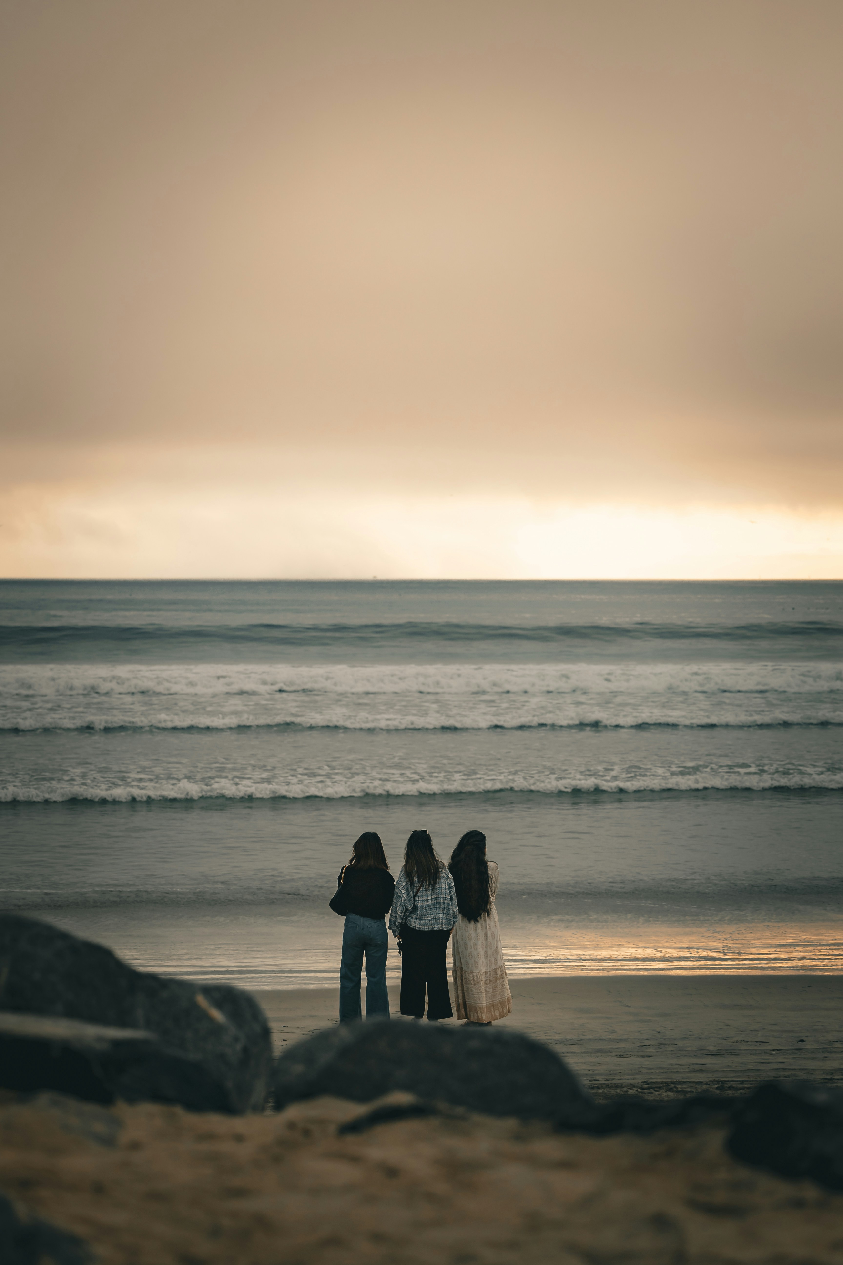 Three women watch the ocean at sunset