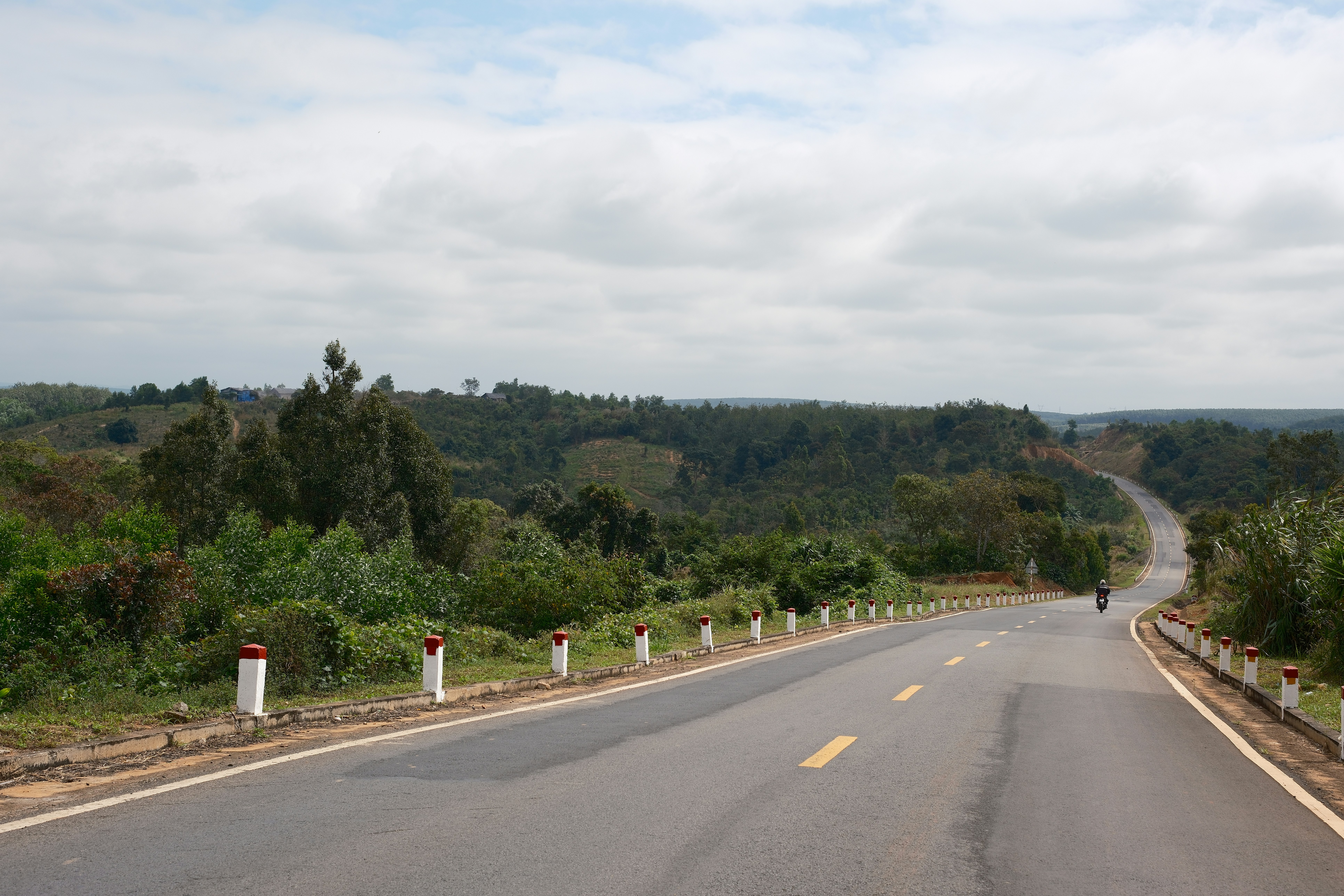 A road winds through lush green hills under a cloudy sky.