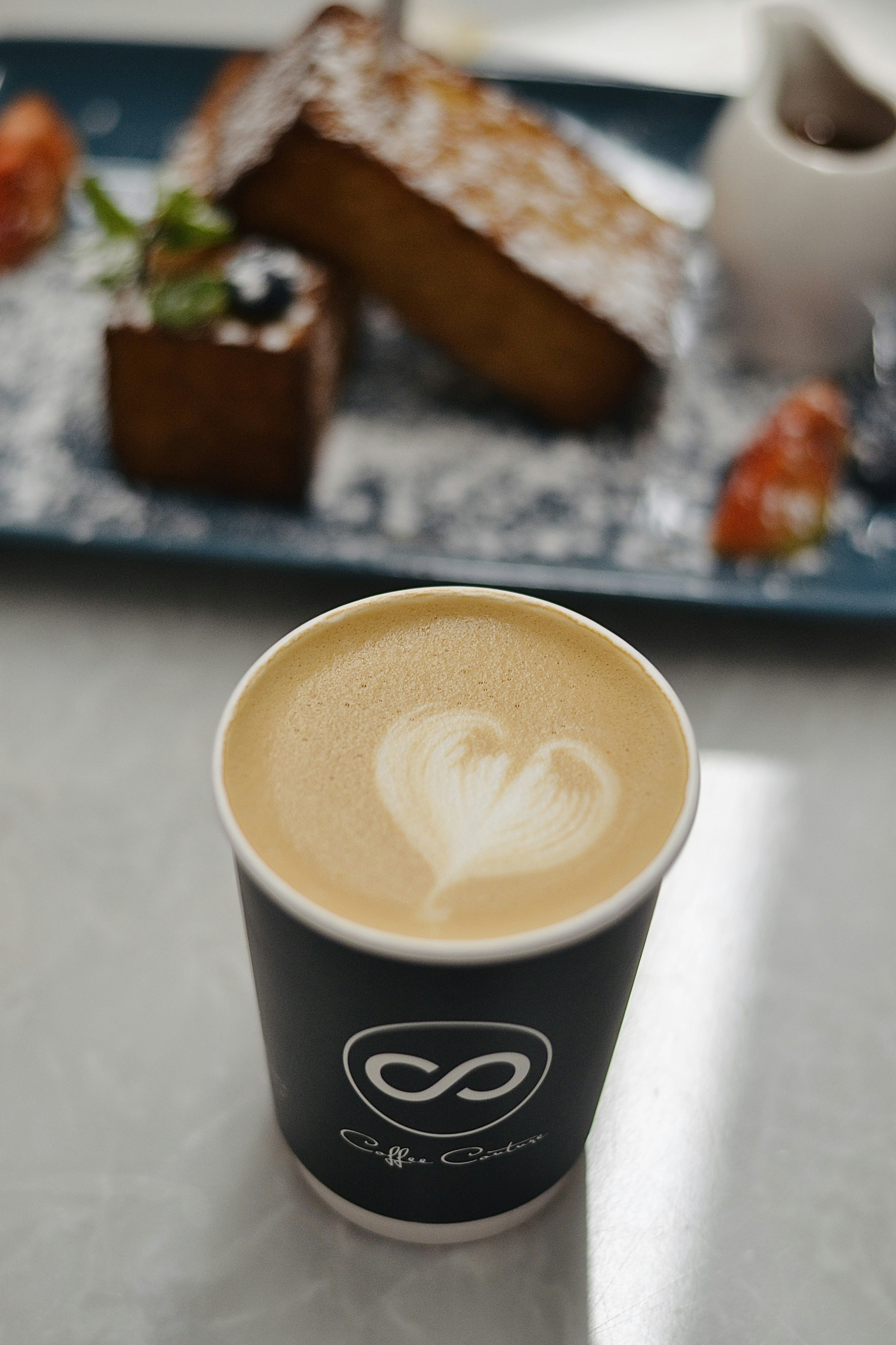 Latte with heart art and delicious dessert on a plate.