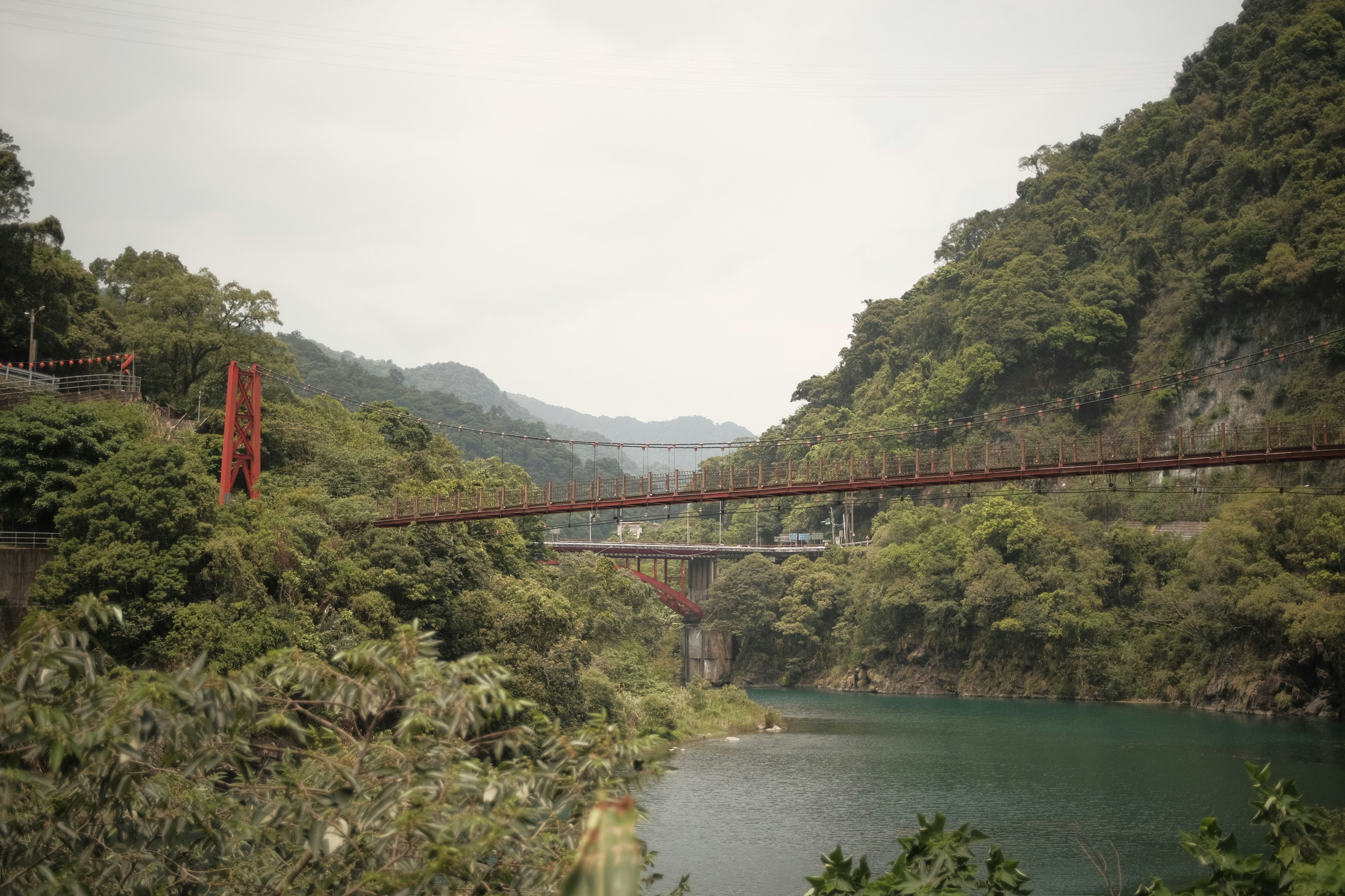 Bridges cross a river between lush, green mountains.