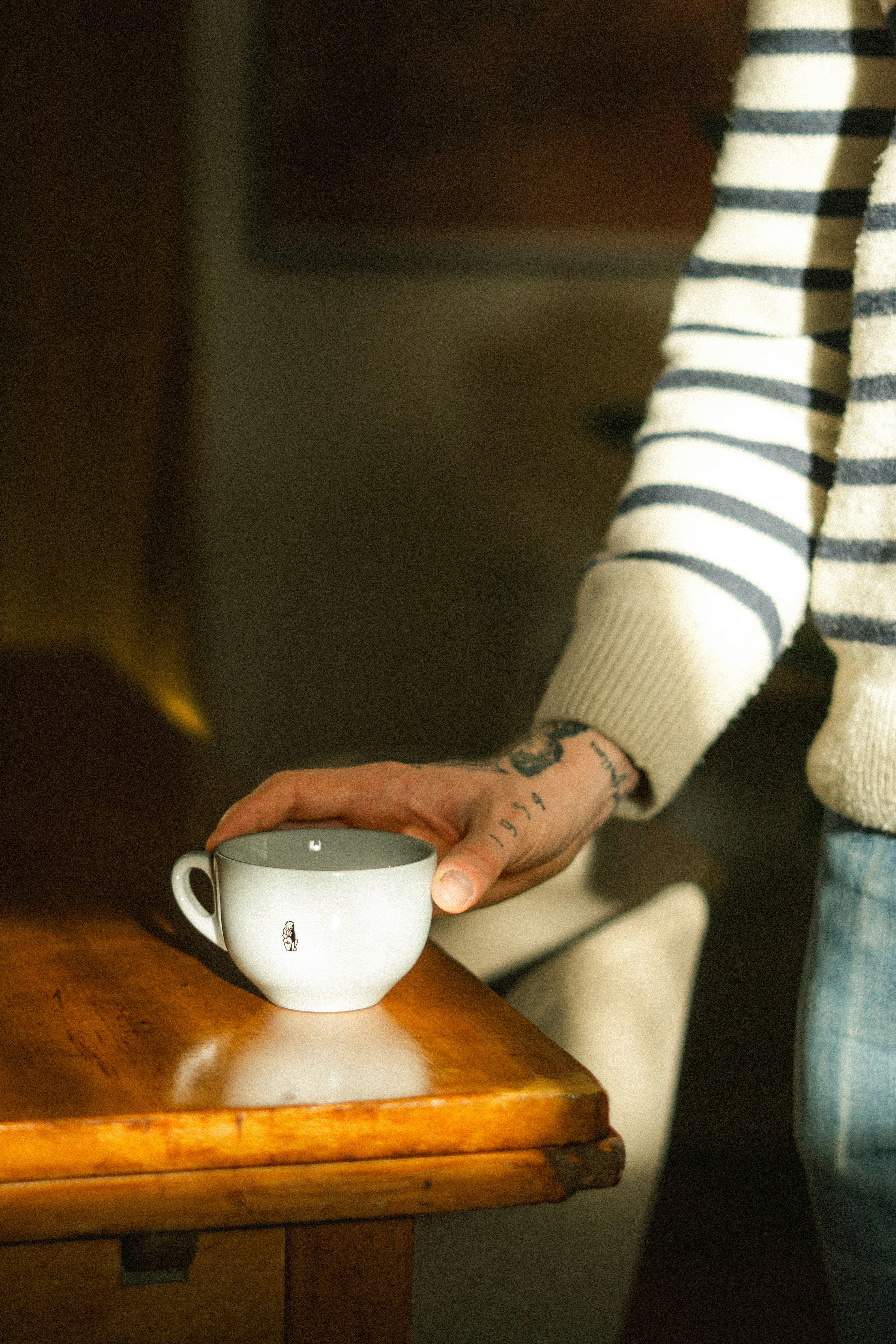 A person holds a cup on a wooden table.