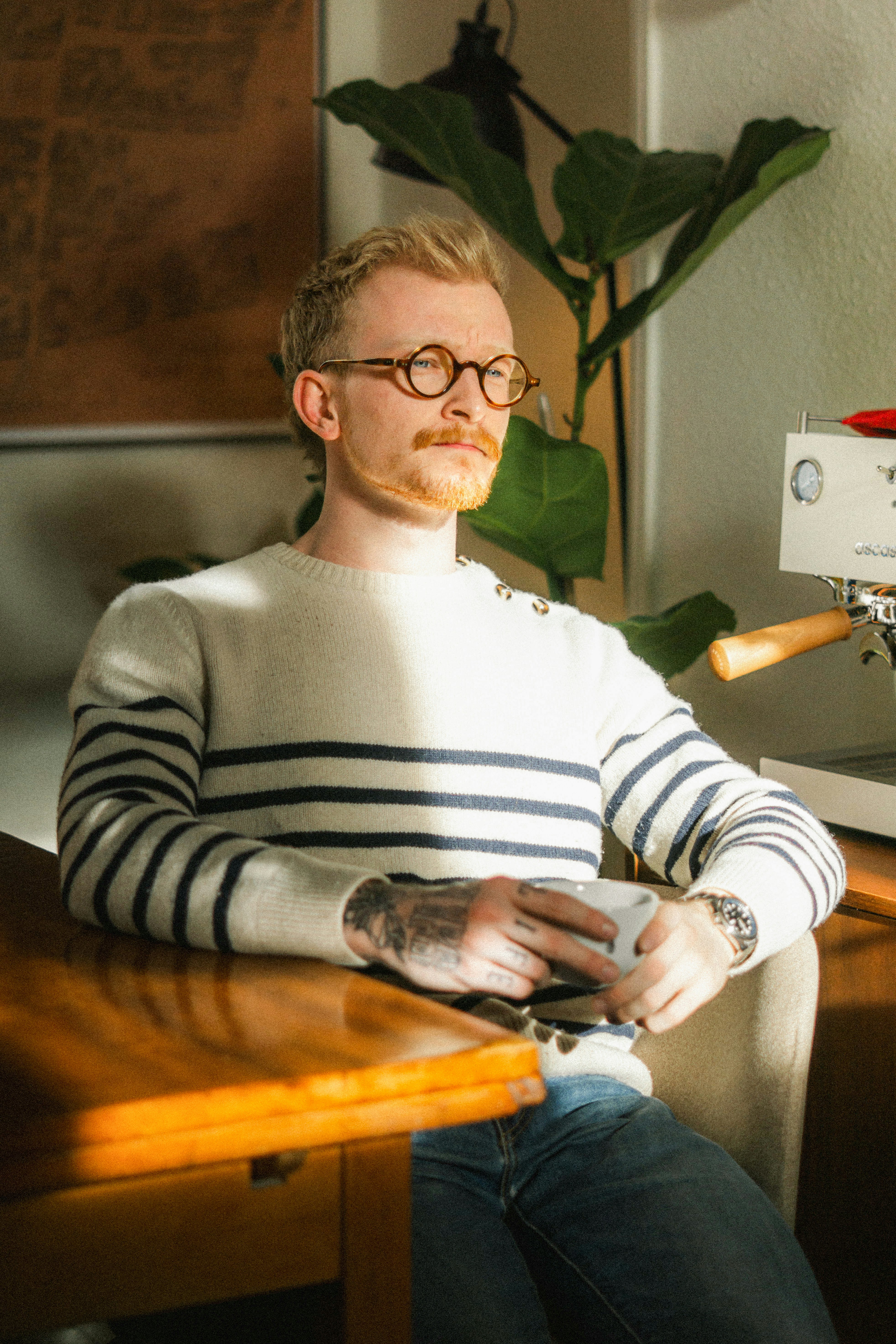 A man sips coffee, sitting near a table.