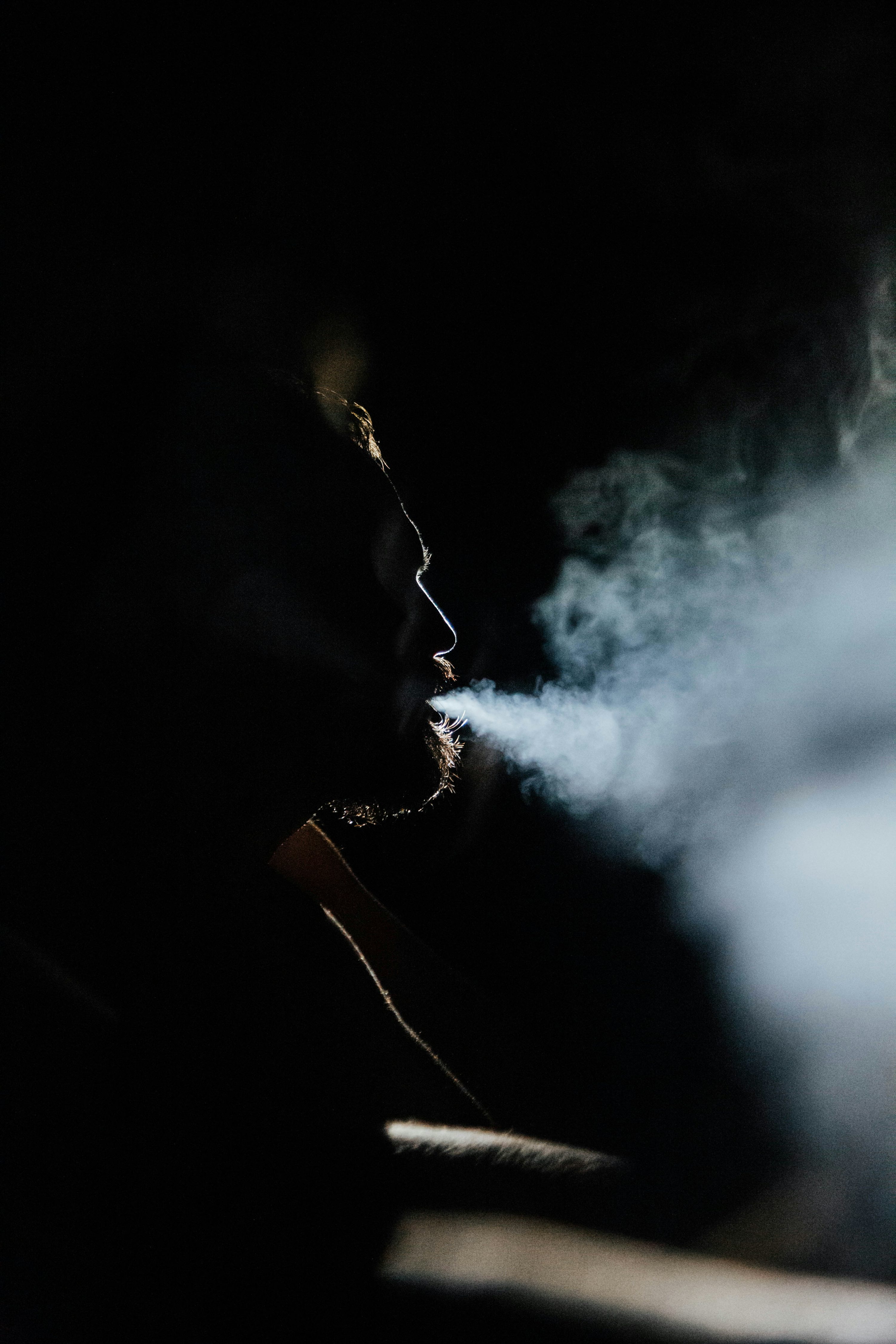 Man exhales smoke in a dimly lit environment. photo – Free Dark Image on Unsplash