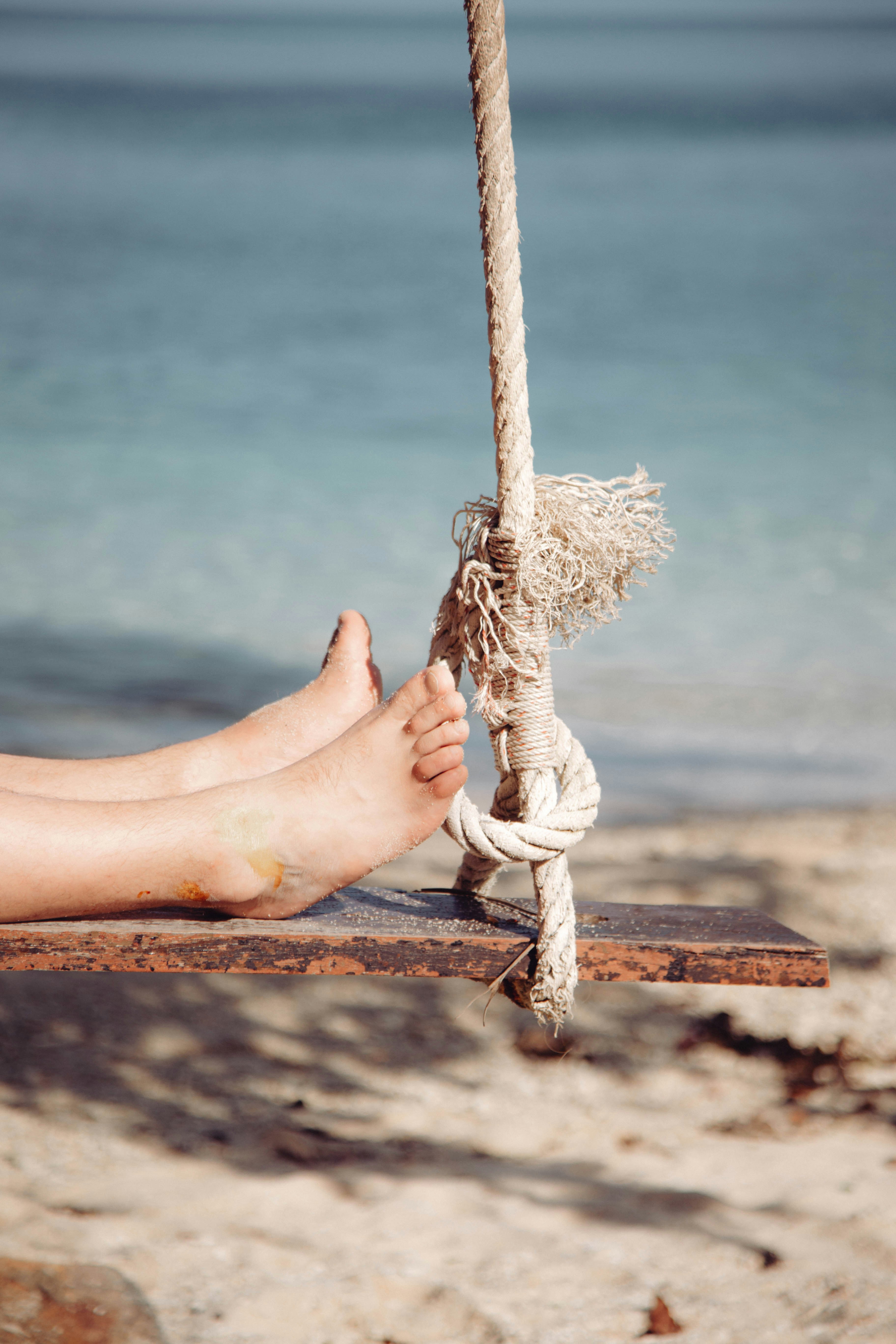 Feet relax on a swing by the ocean.