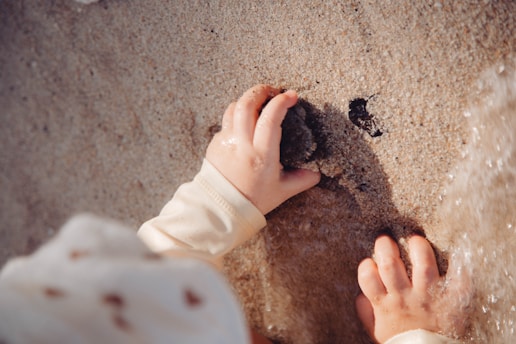 A child's hands play in the sand.
