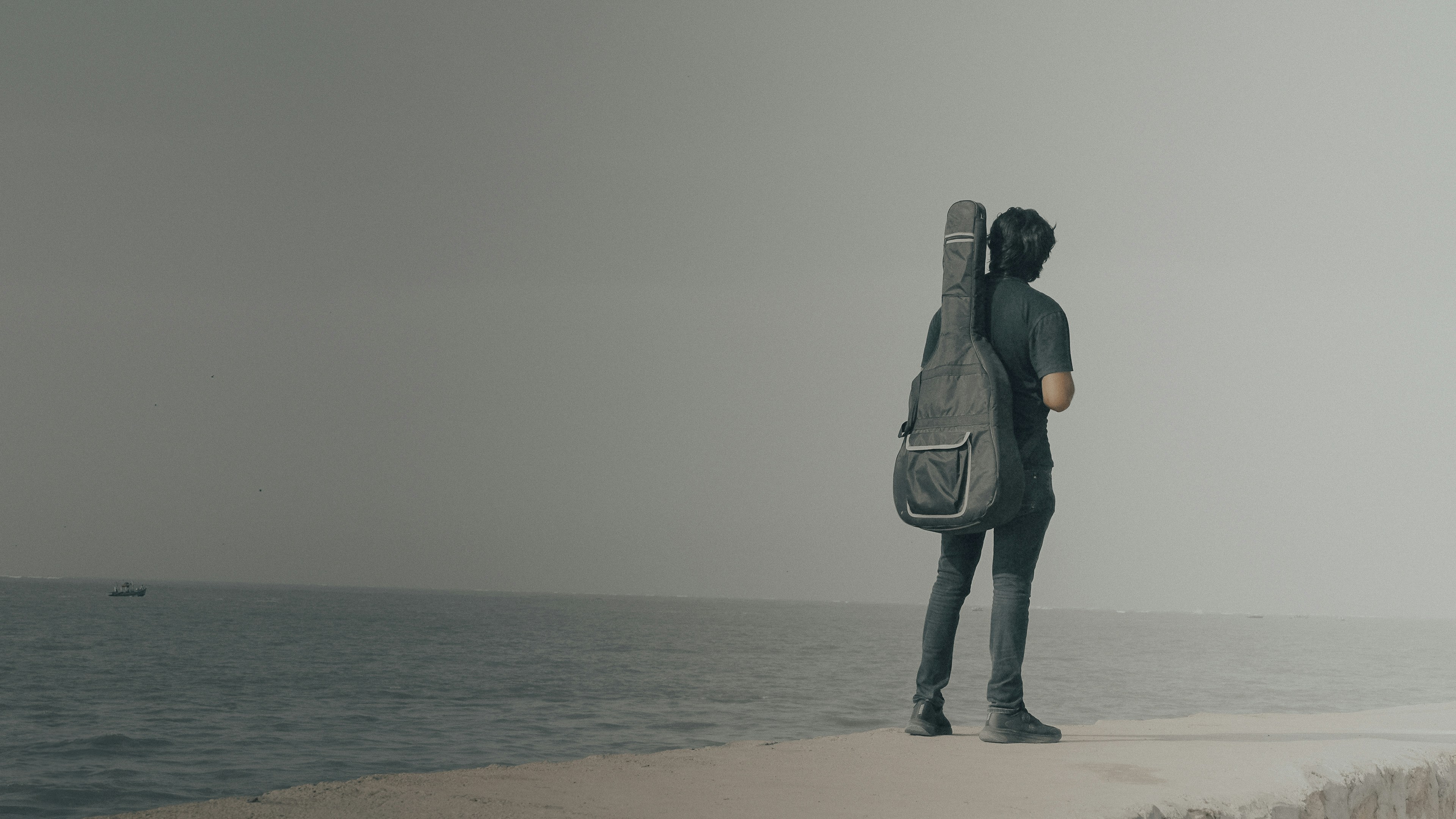 Lone man with guitar looking at sea