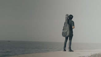 A person stands by the sea with a guitar.