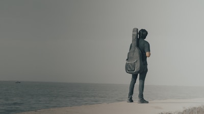 A person stands by the sea with a guitar.