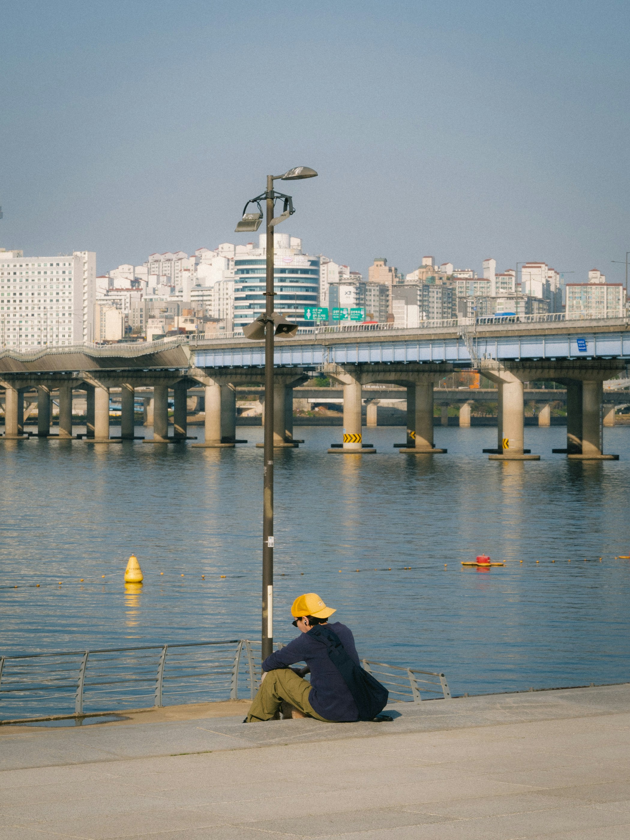 Eine Person sitzt am Wasser und blickt auf die Stadt.