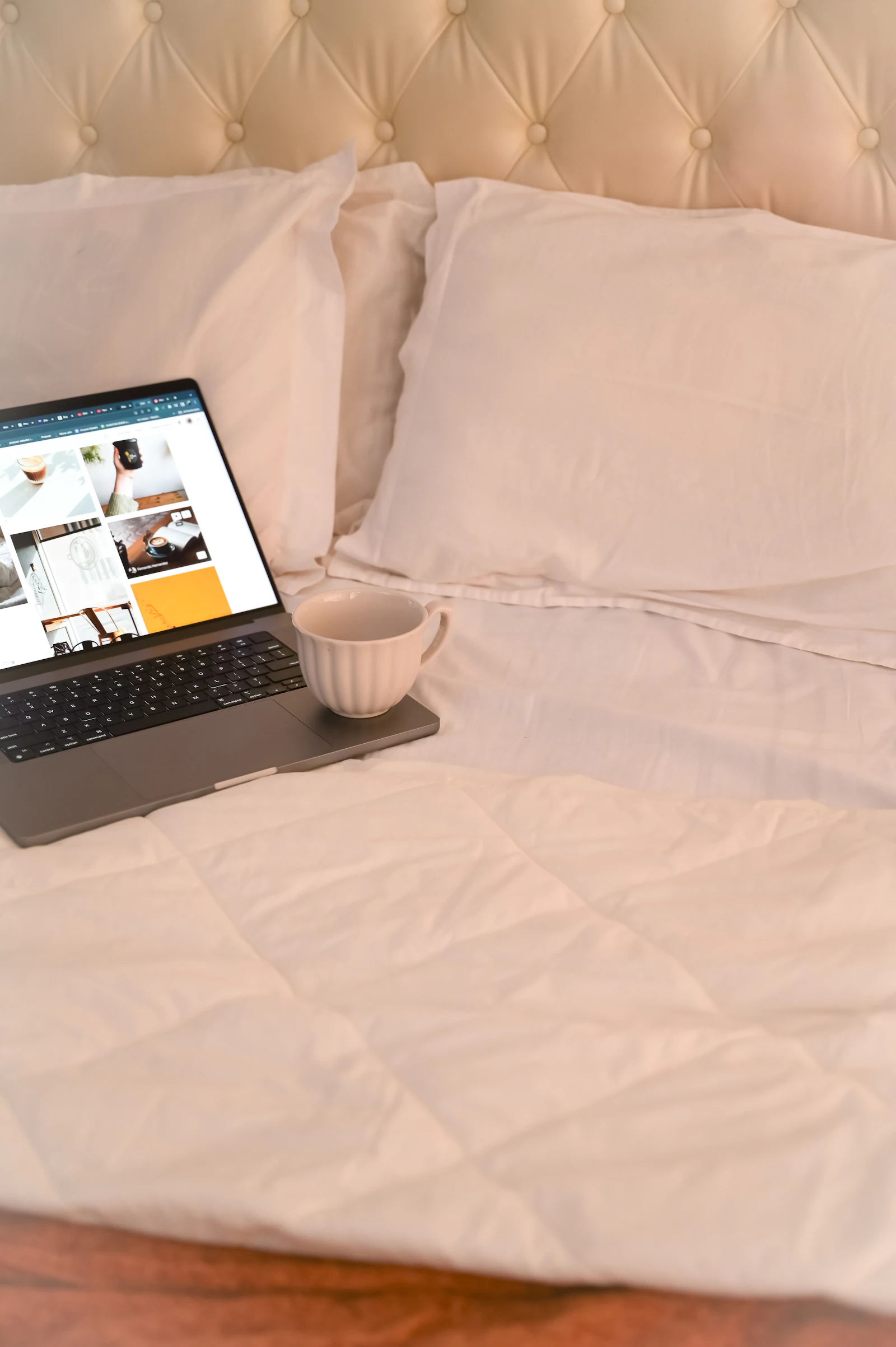 Laptop and a warm beverage on a bed in soft natural light