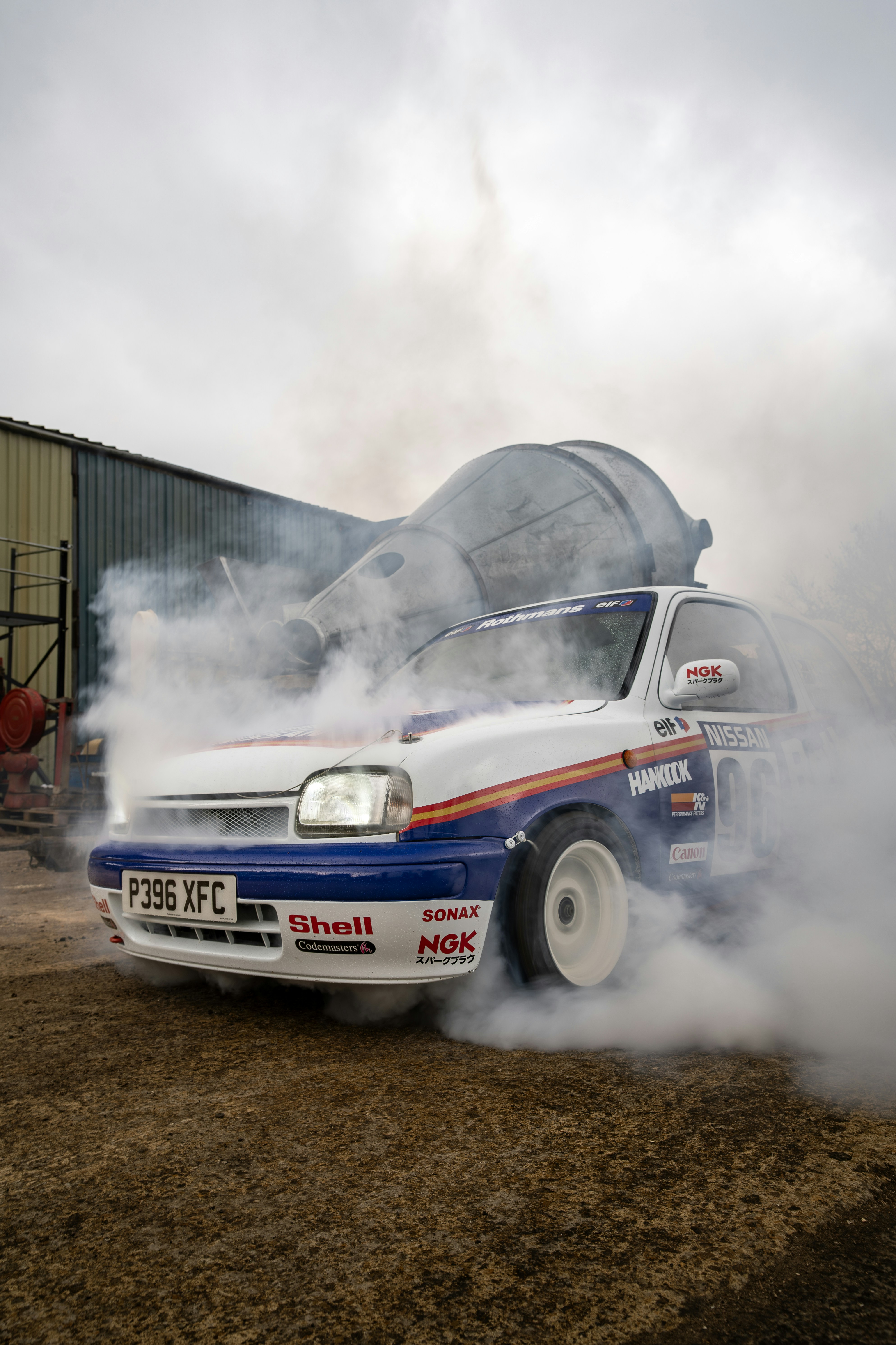 A rally car drifts, kicking up a cloud of smoke.