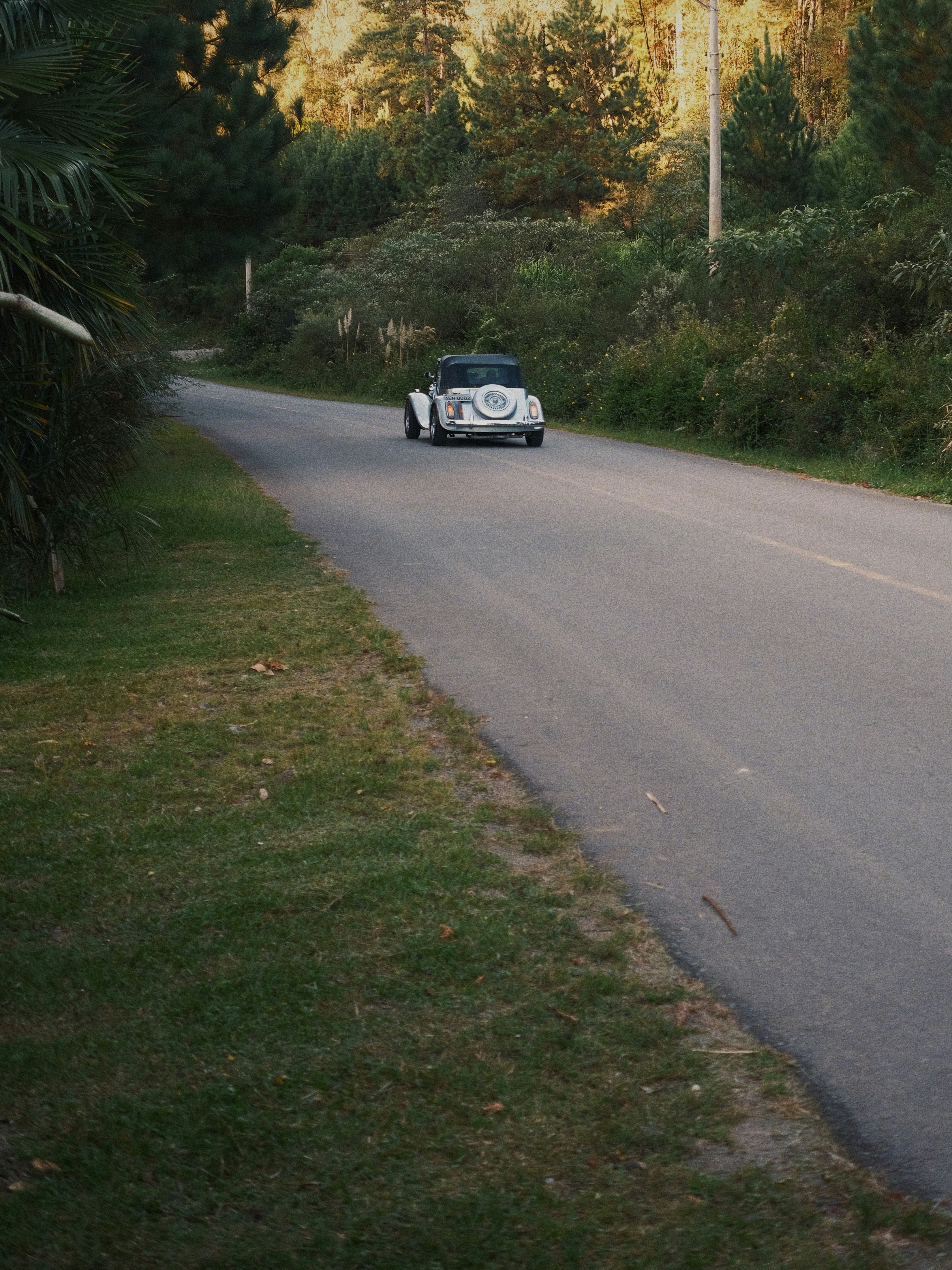 A classic white car drives down a rural road.