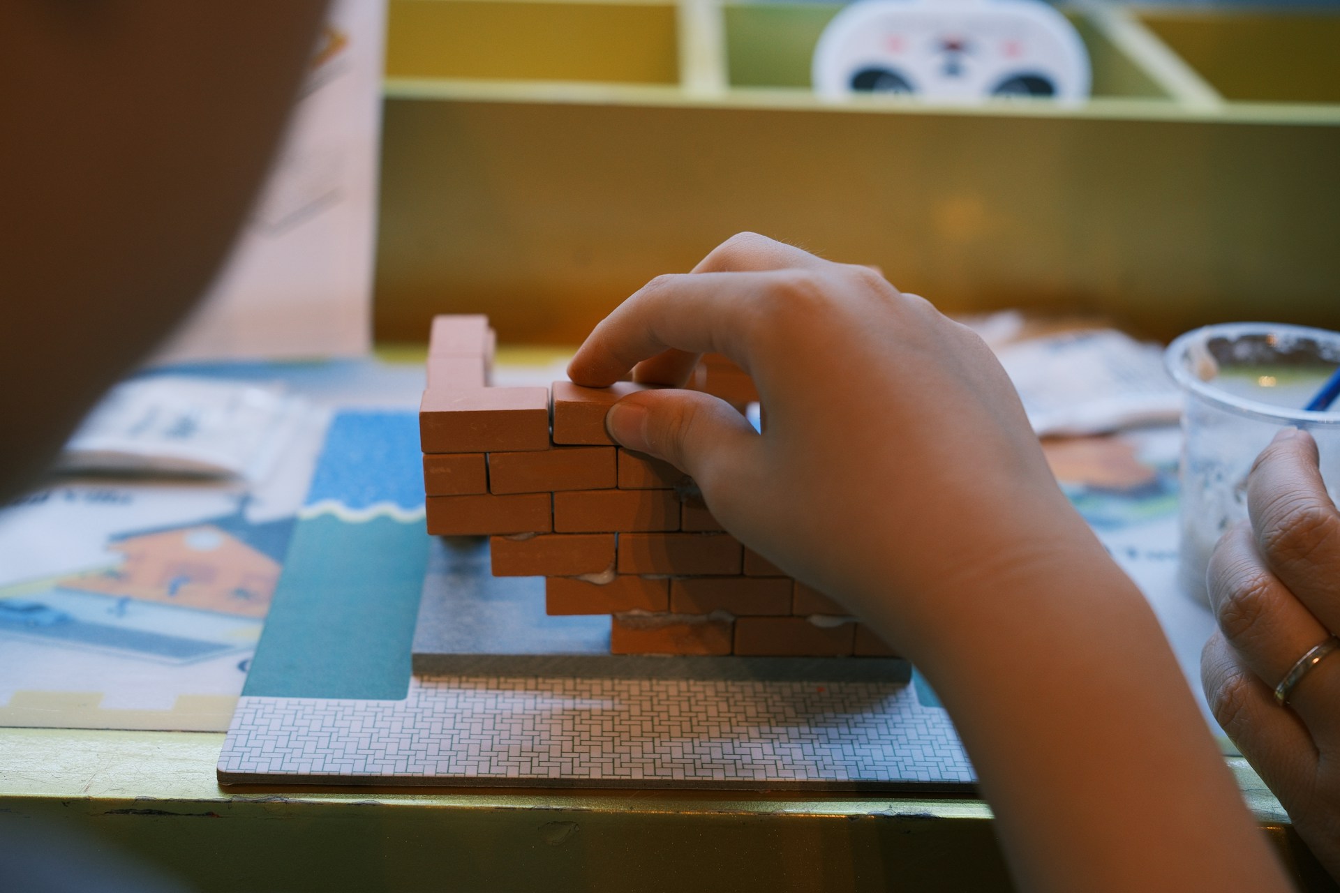 A hand builds a miniature brick structure.