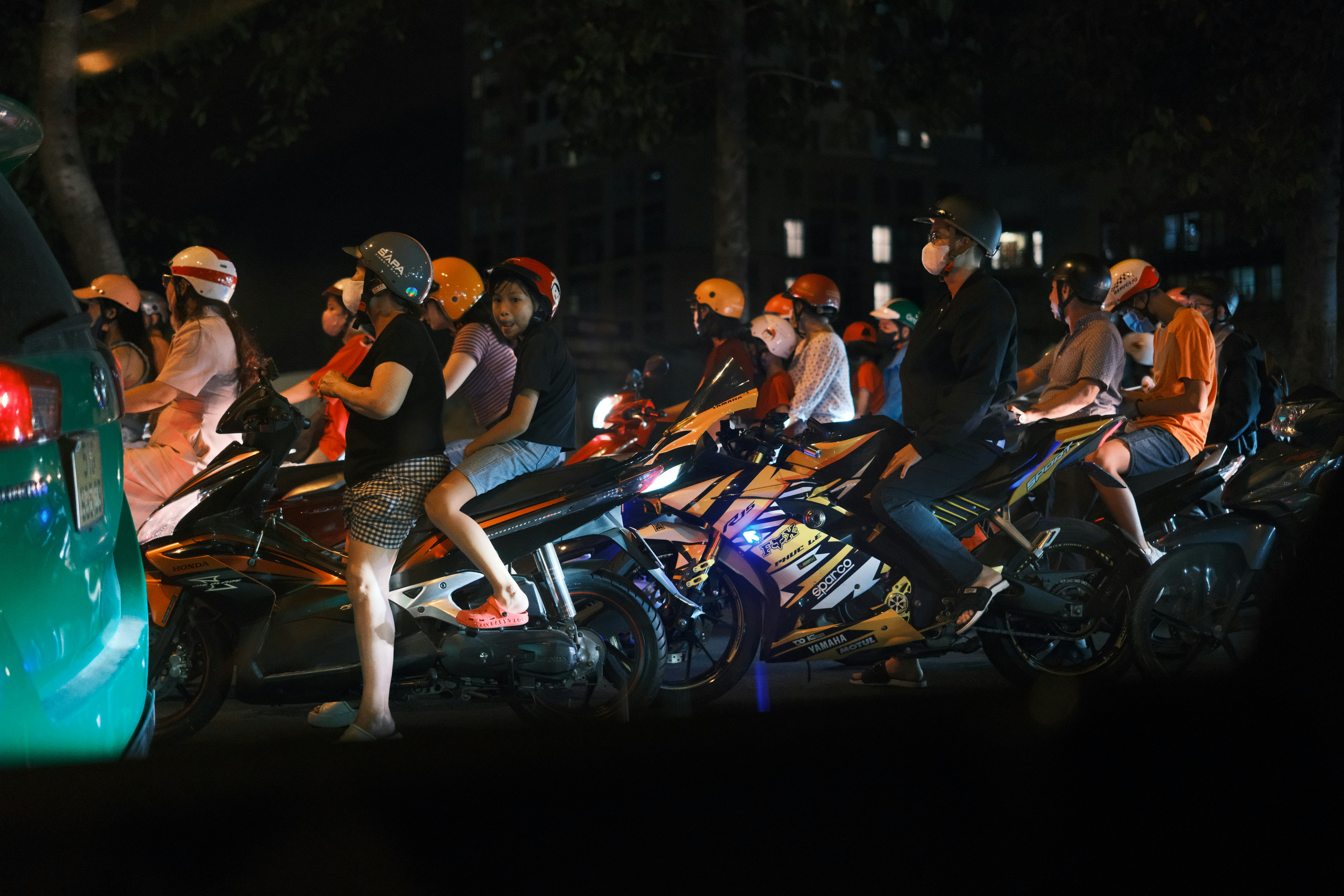 Pengendara sepeda motor dihentikan di kemacetan pada malam hari.