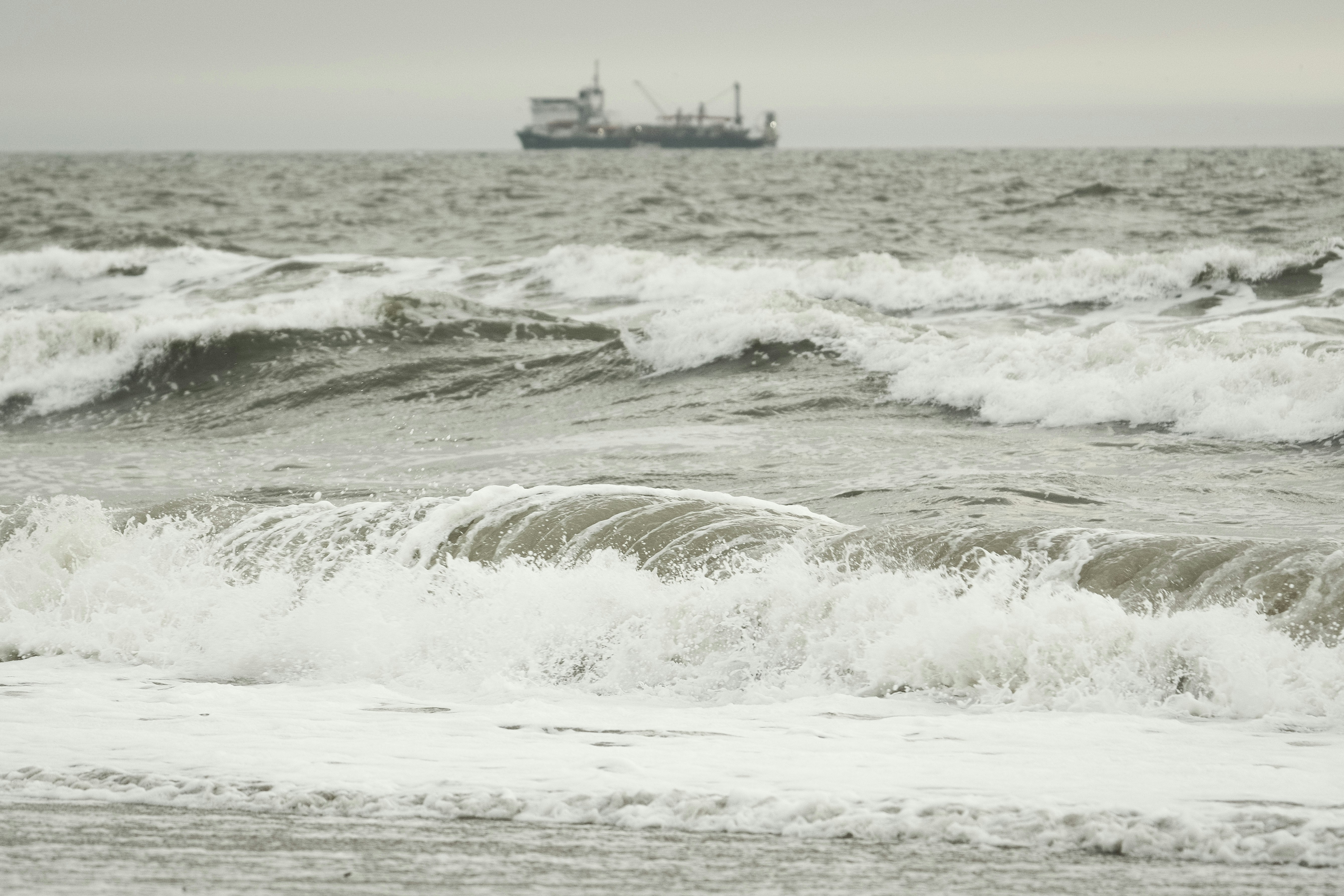 Waves crash in the sea with a distant ship.
