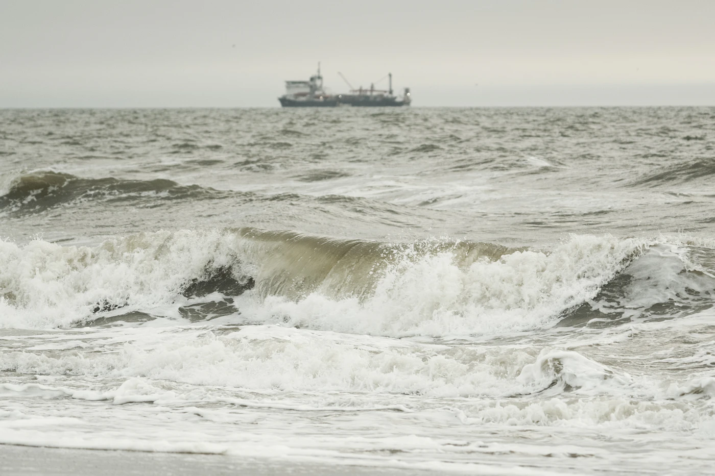 Rough ocean waves with a distant commercial vessel on the horizon