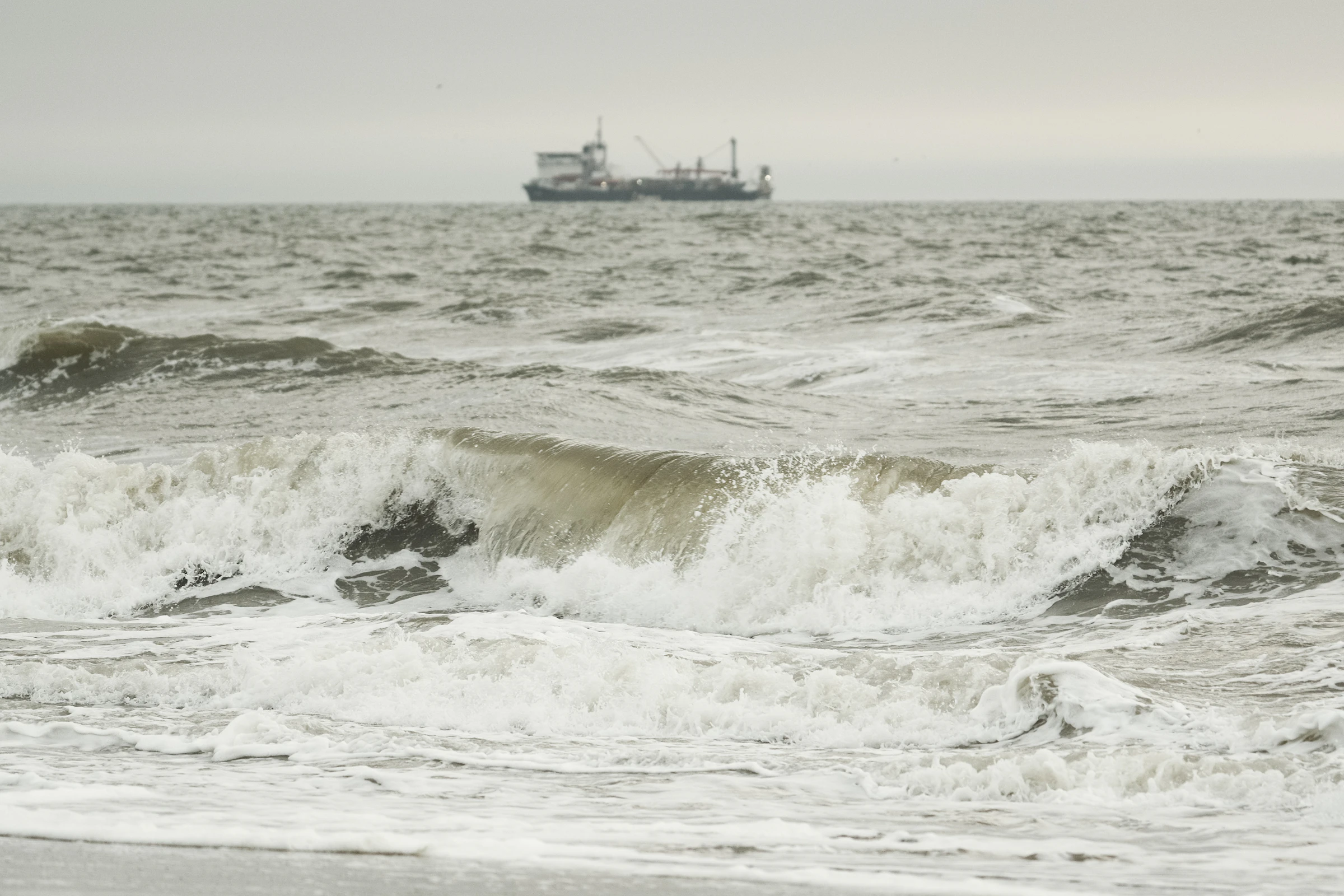 Rough ocean waves with a distant commercial vessel on the horizon