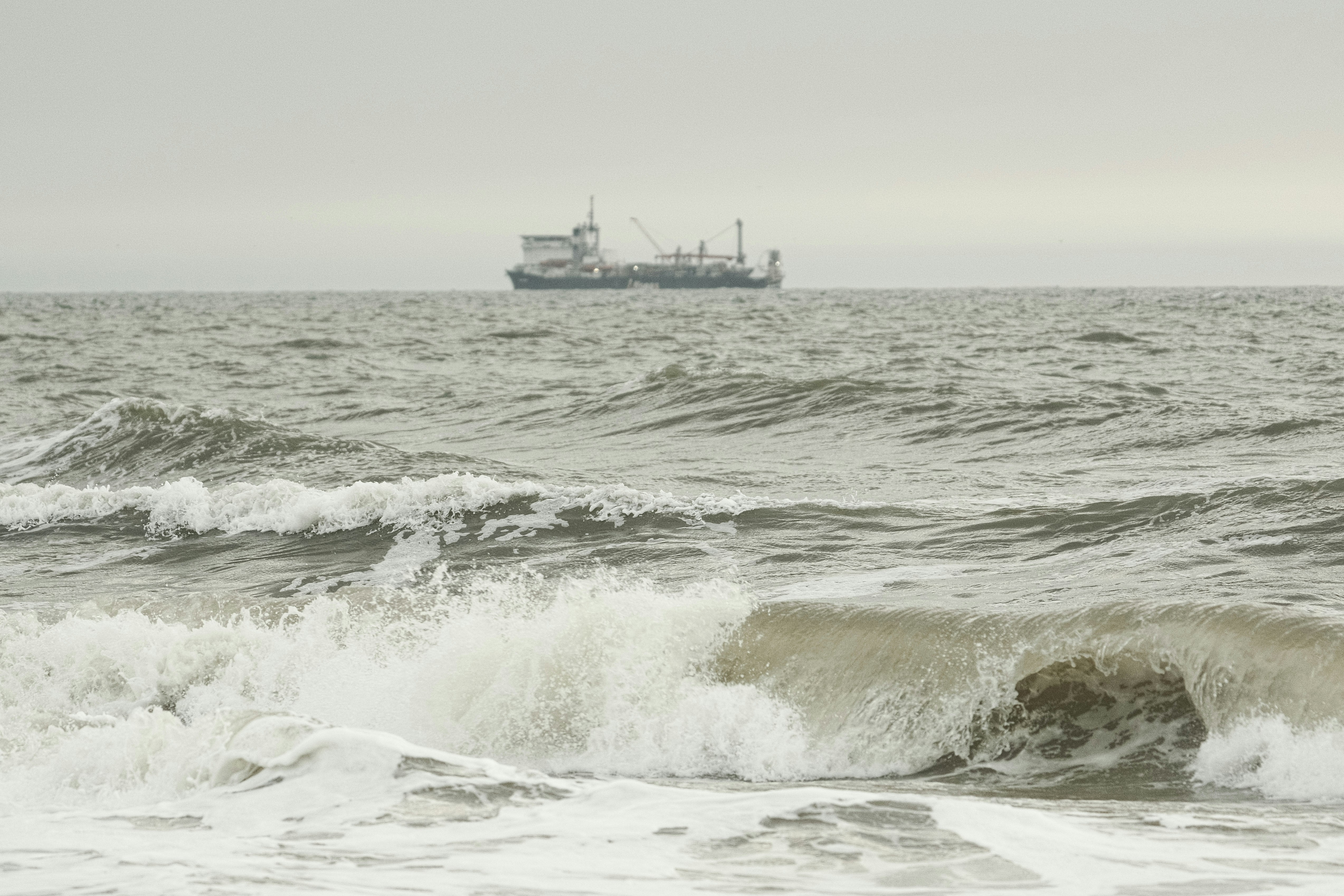Waves crash with a ship in the distance.