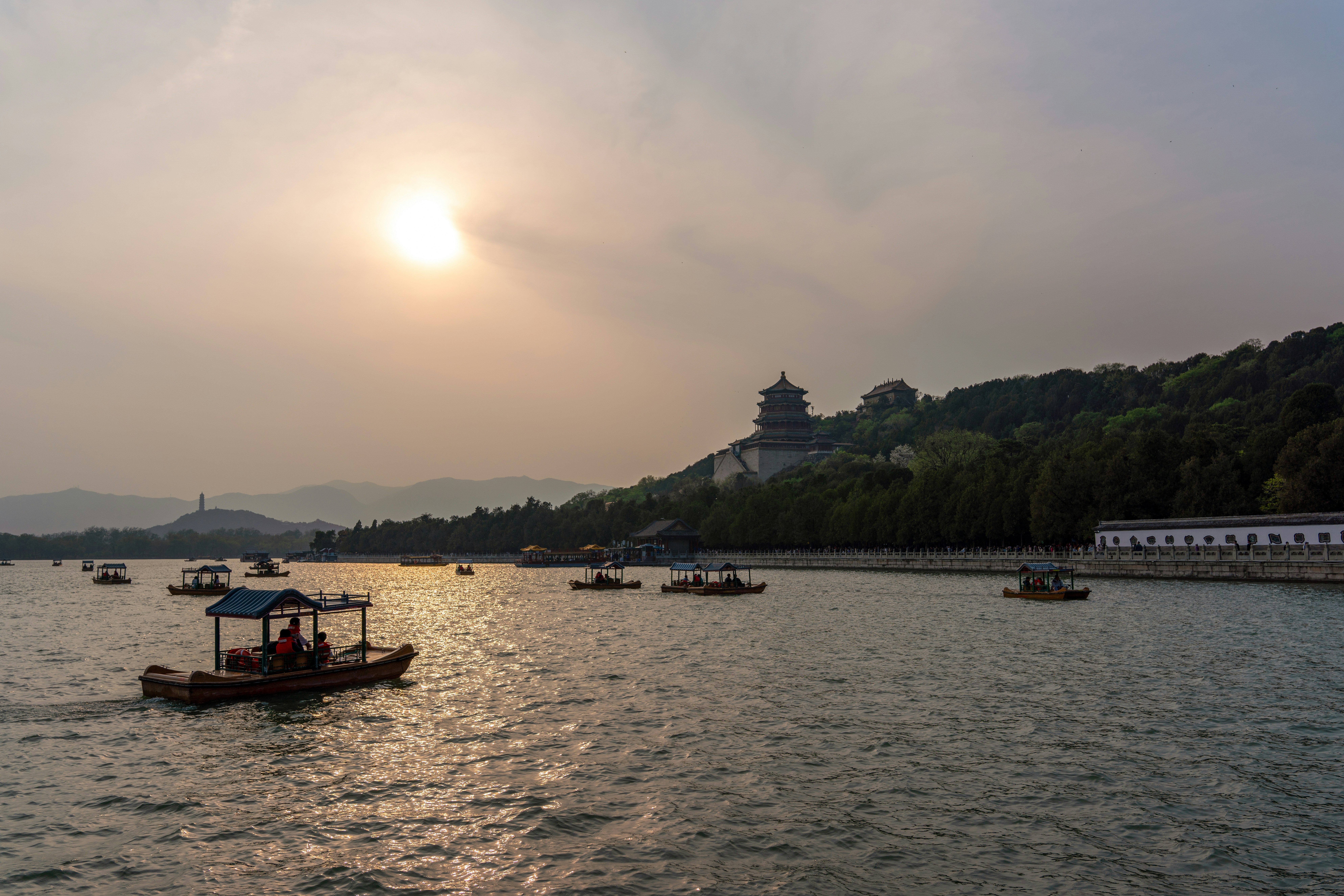 Boats sail on a lake under a setting sun.