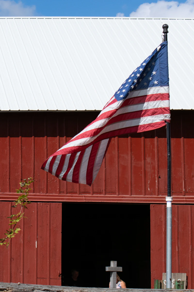 An American flag waving in front of a red wooden barn