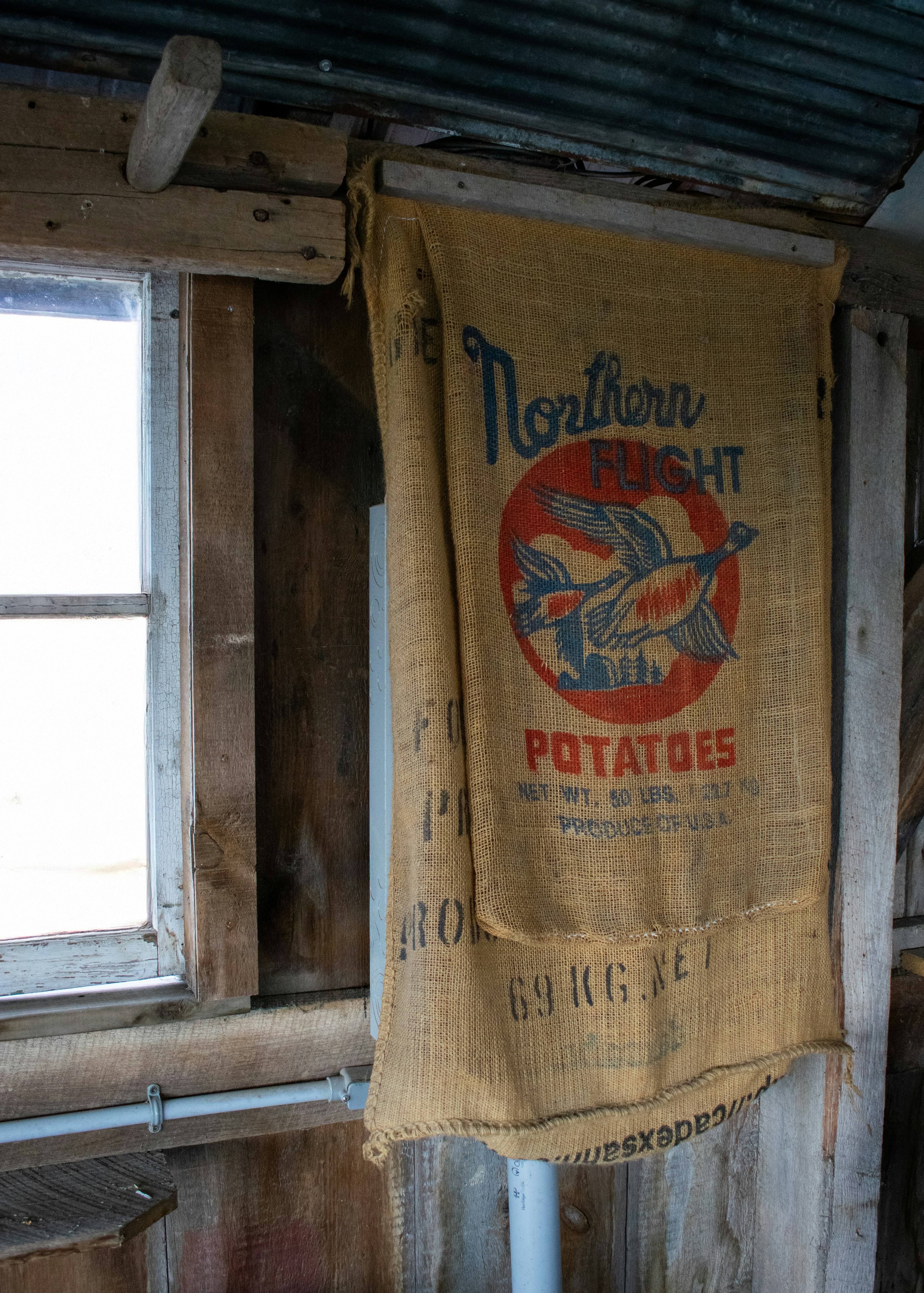 Old potato sack hangs in a rustic window frame.