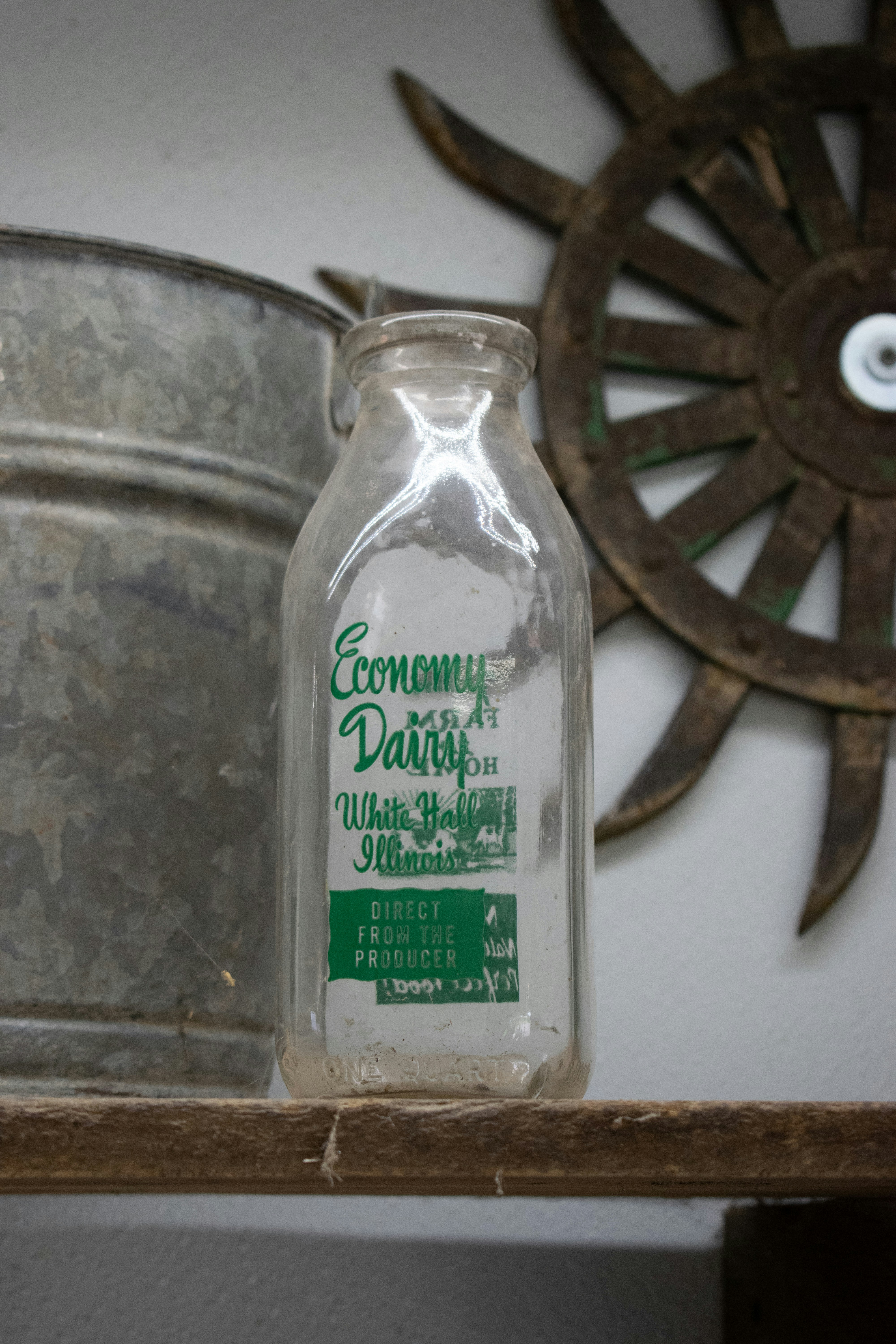 An antique milk bottle sits on a wooden shelf.