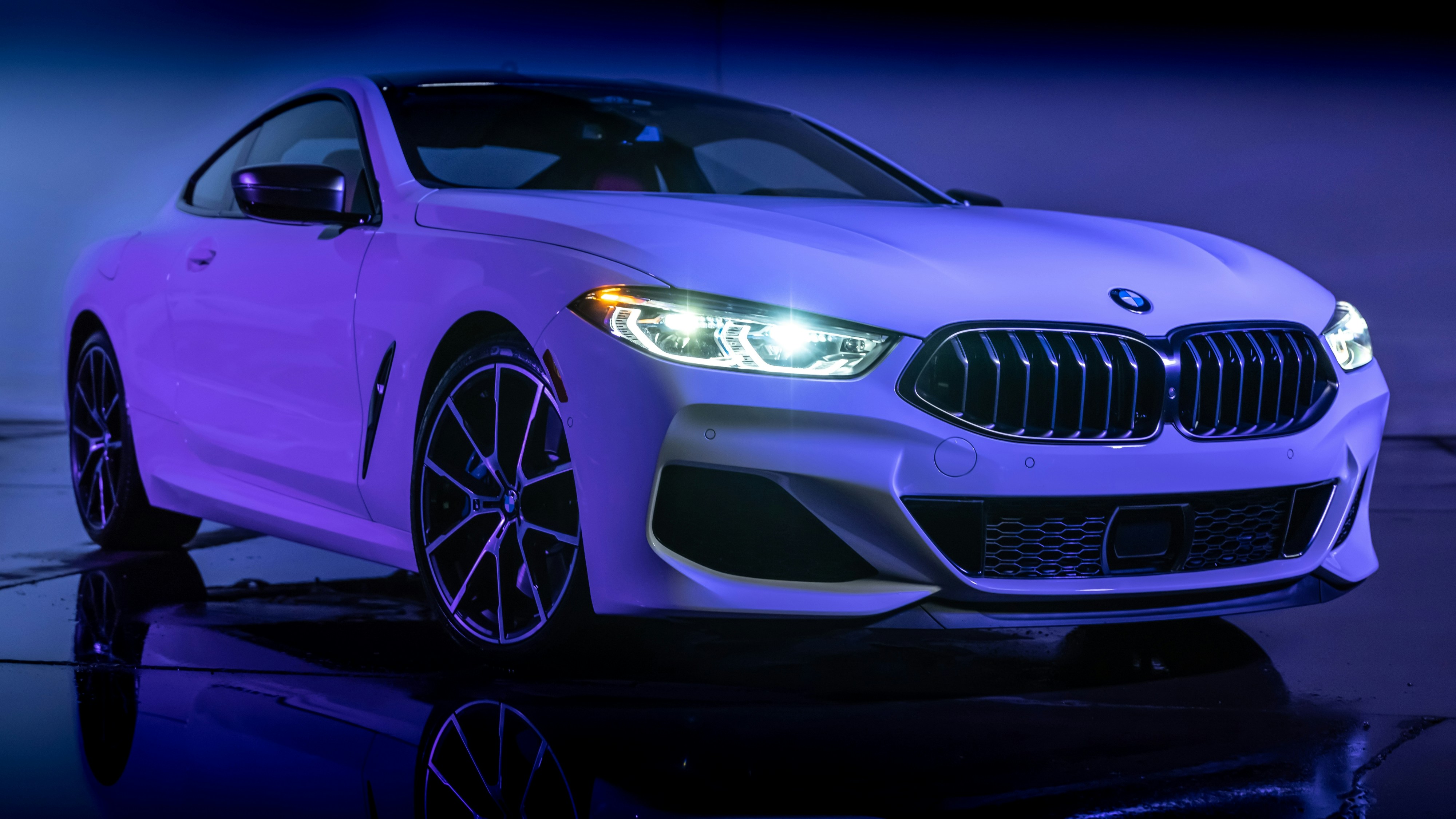A white BMW car is illuminated in blue light.