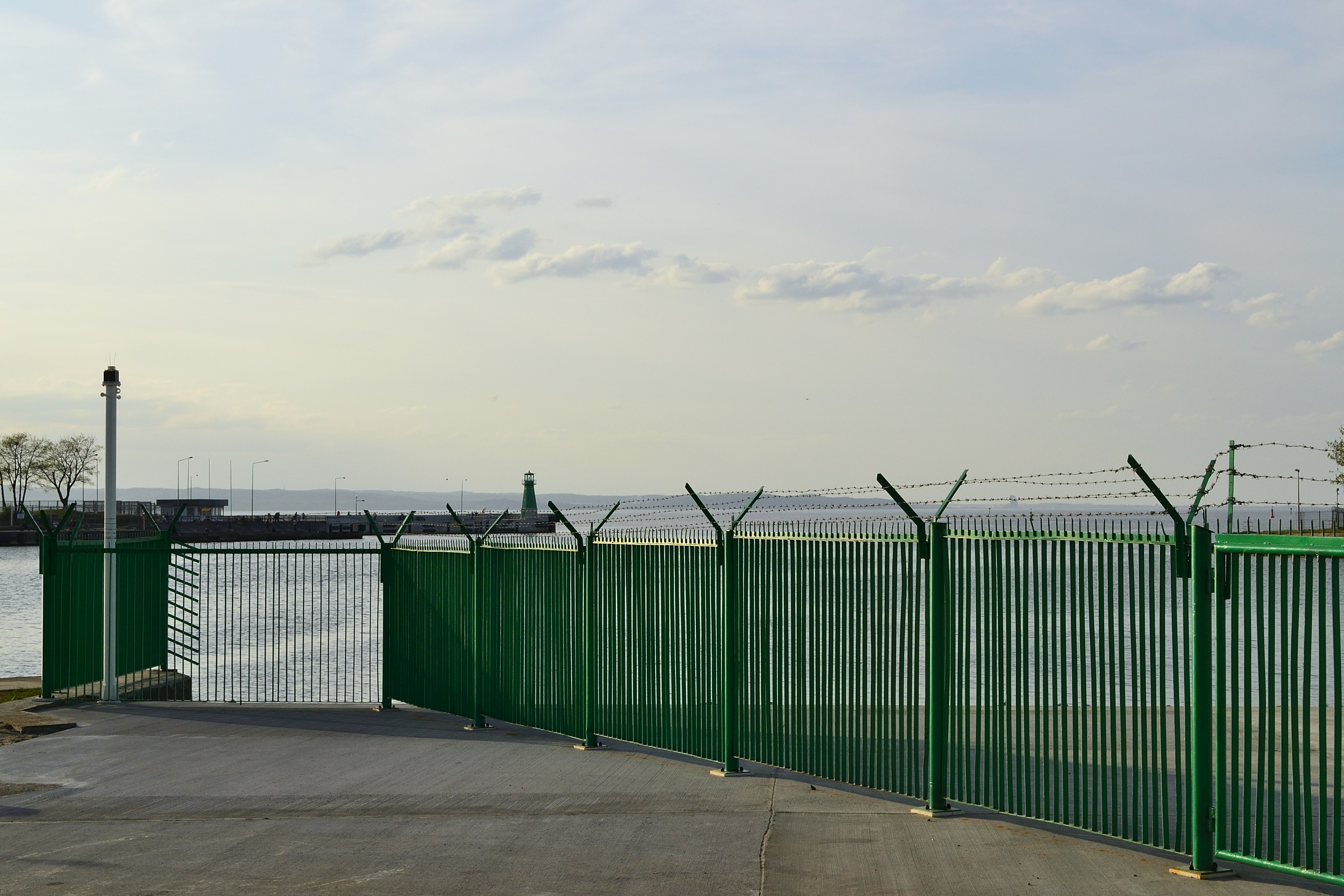 Green fence with barbed wire by water.