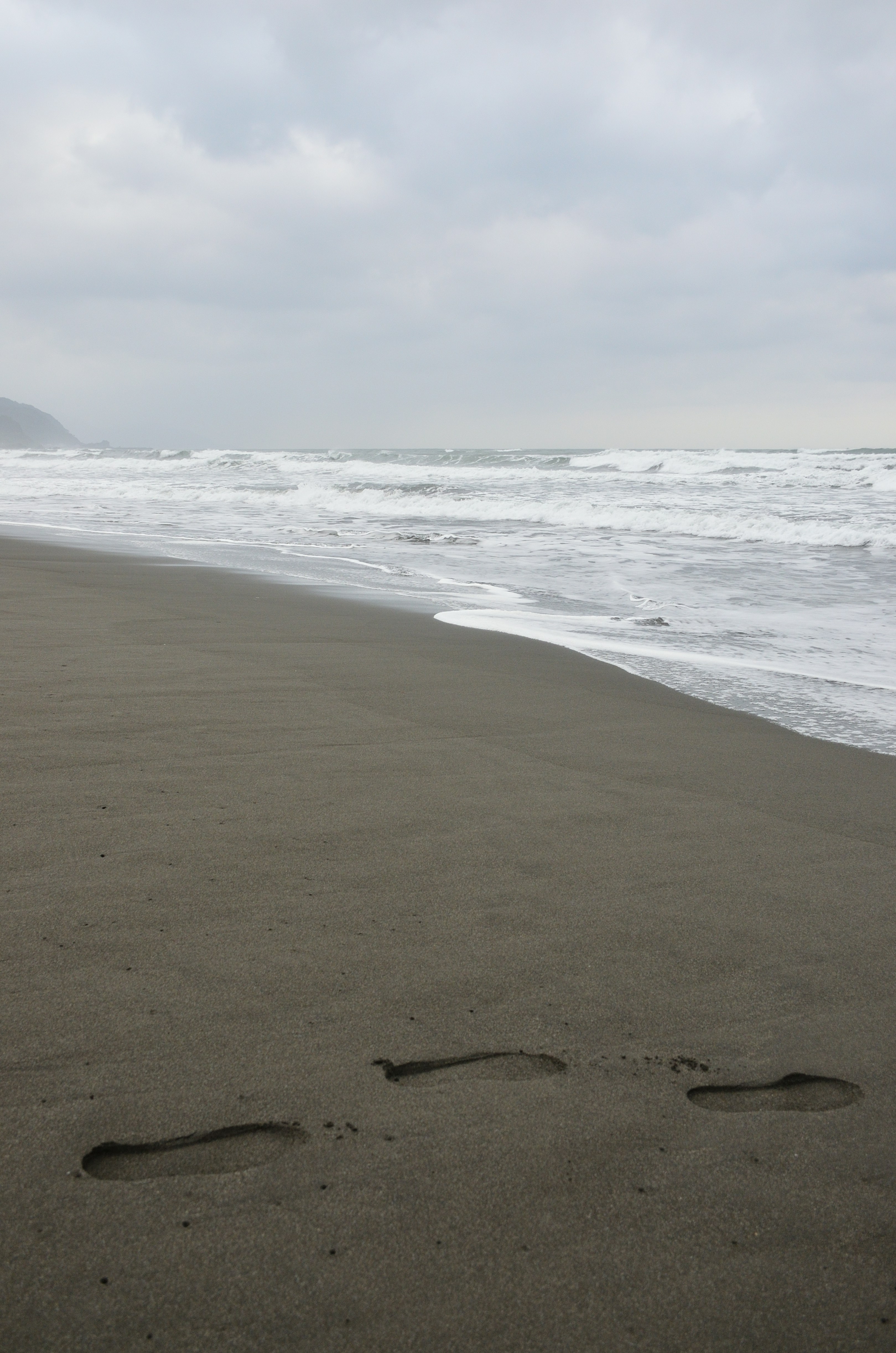 Footprints lead along a beach beside the ocean.