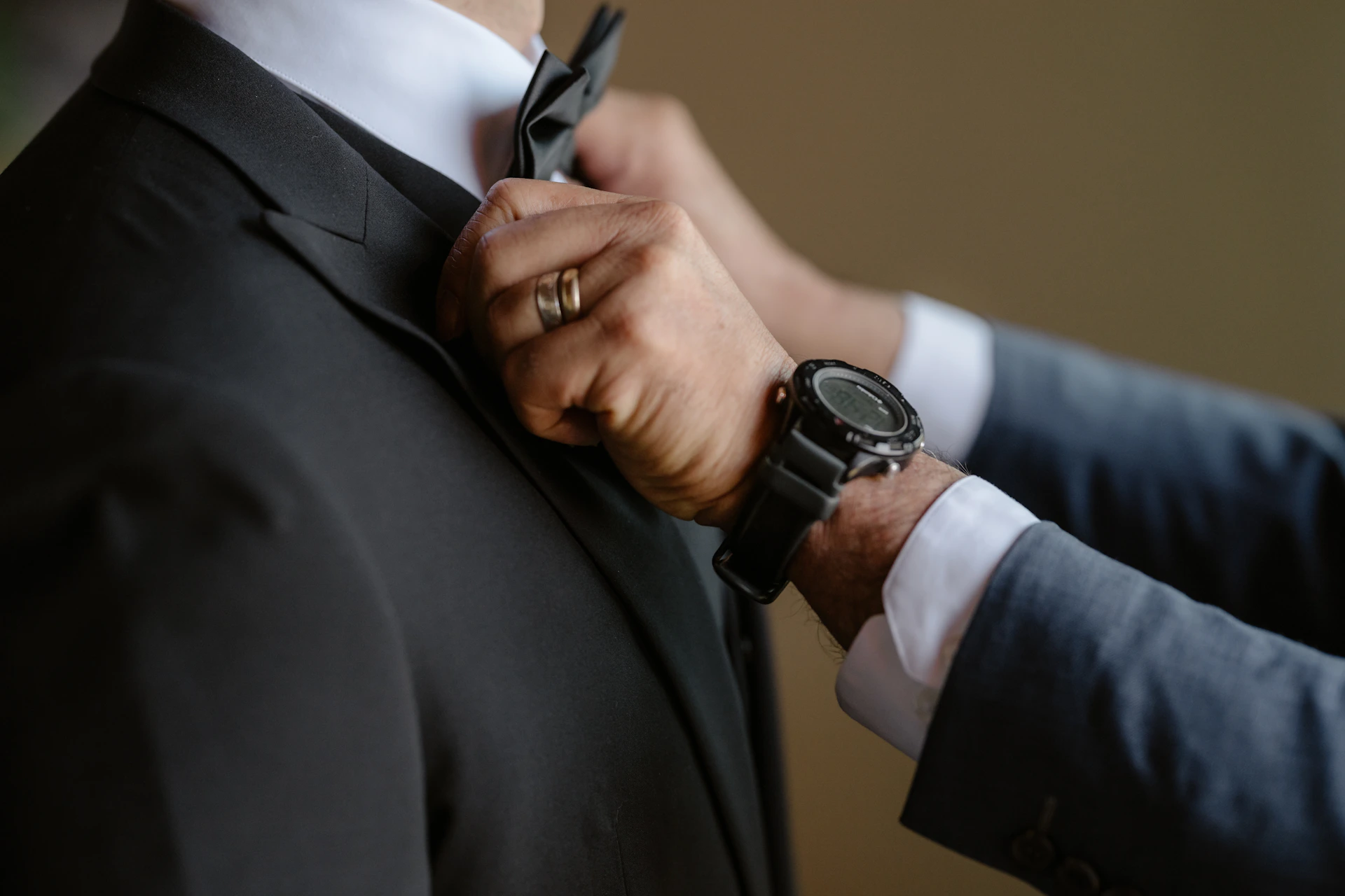 A man adjusts a bow tie on another man.