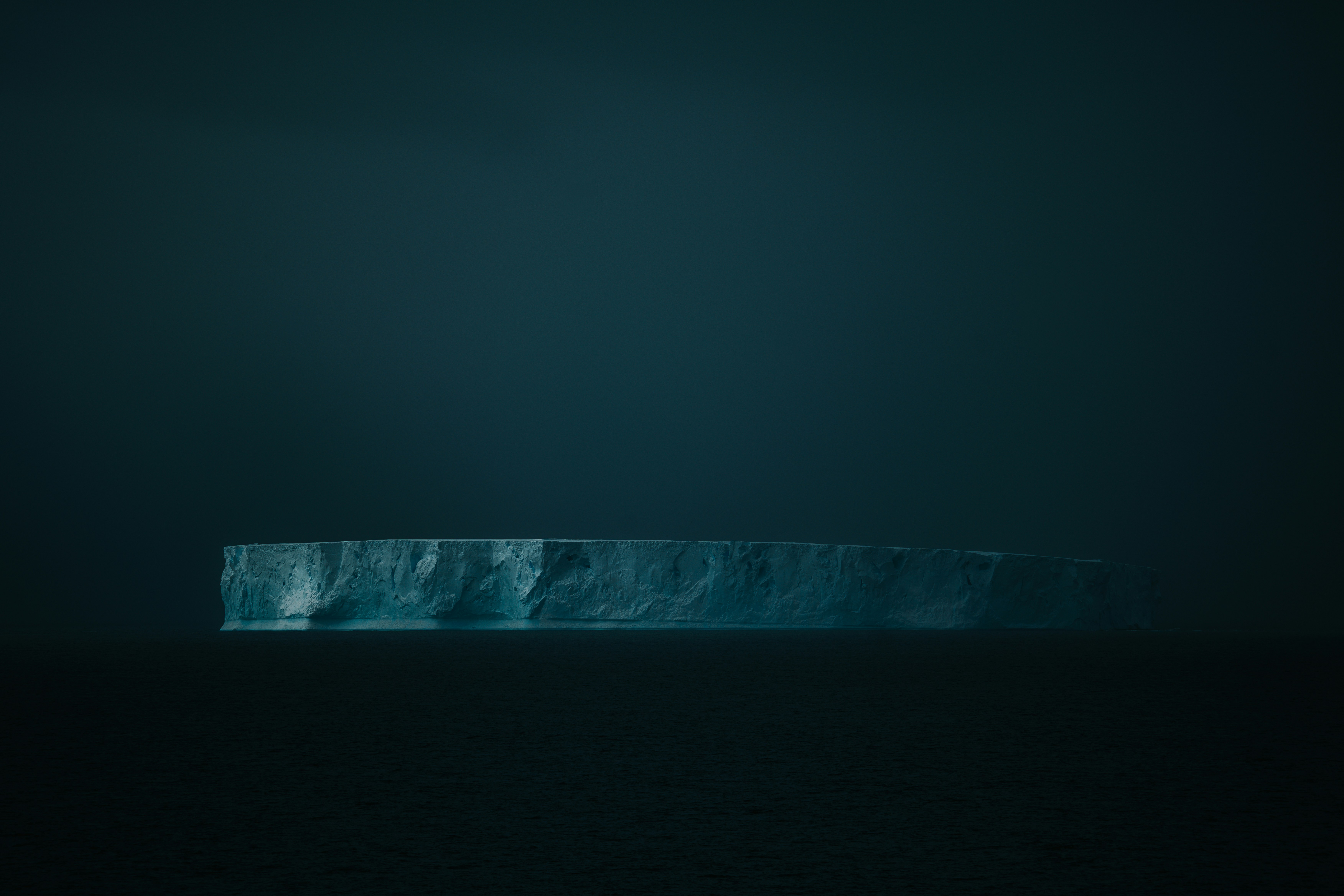 A large iceberg floats alone in dark waters.
