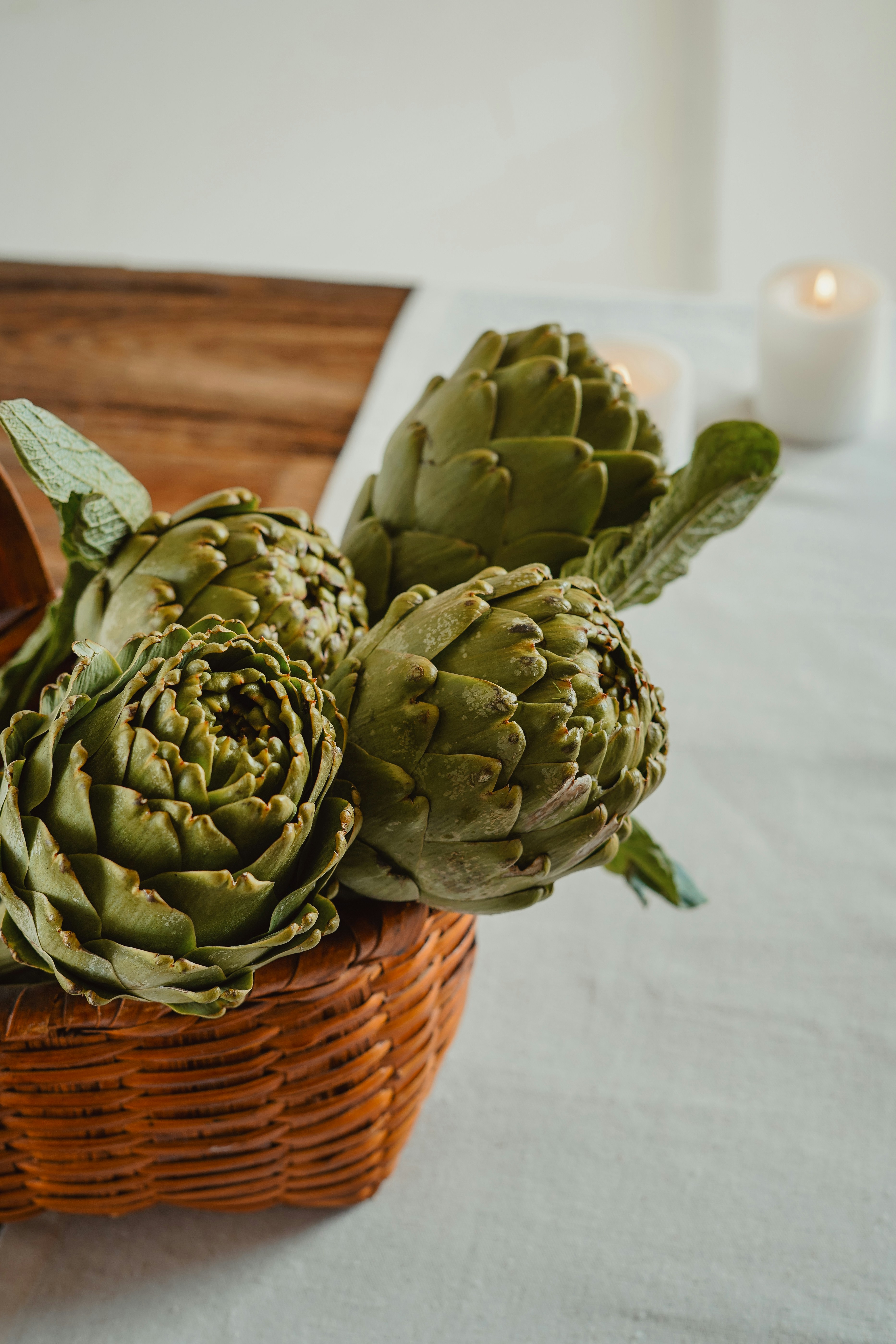 Artischocken sitzen in einem Weidenkorb auf einem Tisch.