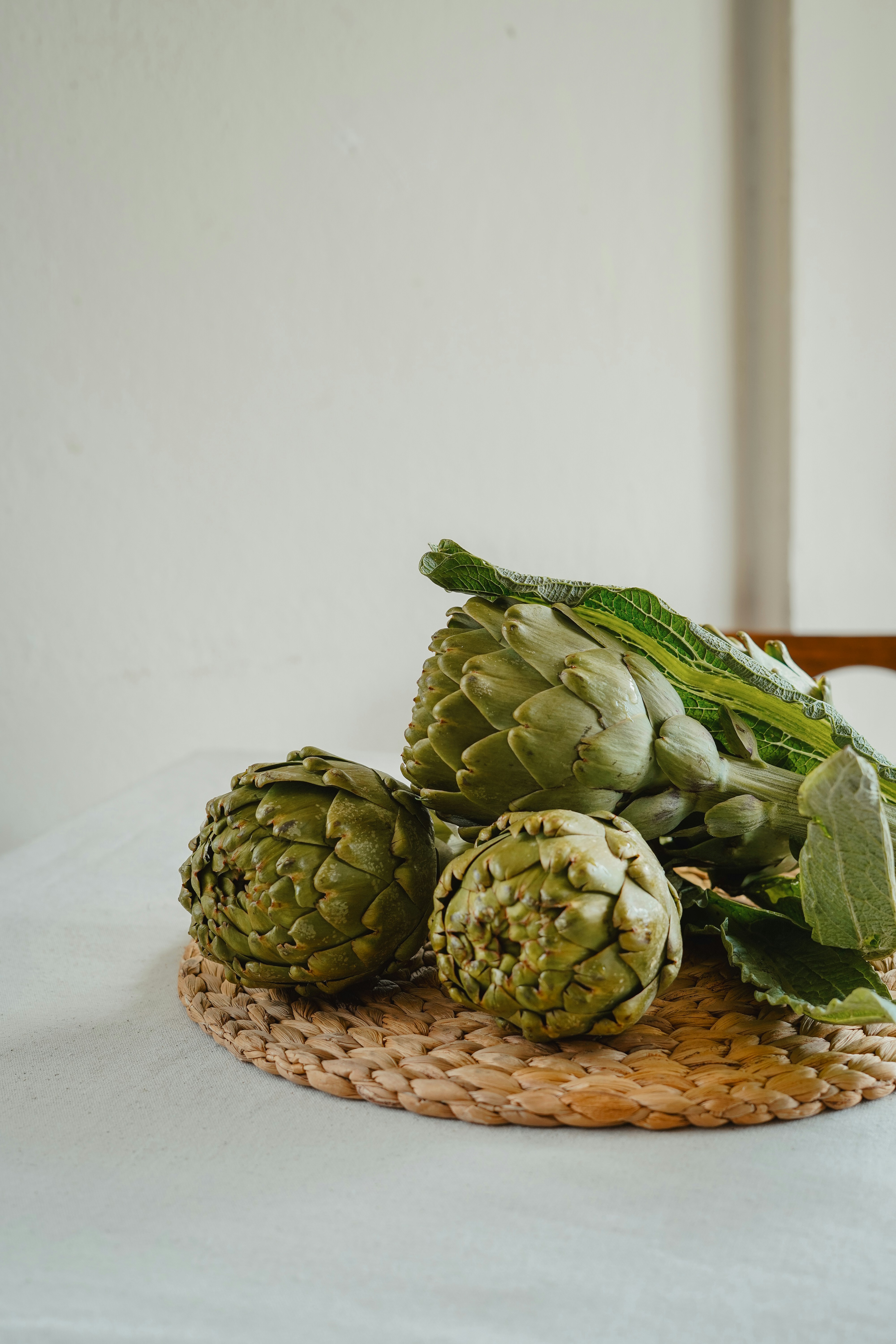 Drei frische Artischocken auf einer gewebten Matte.