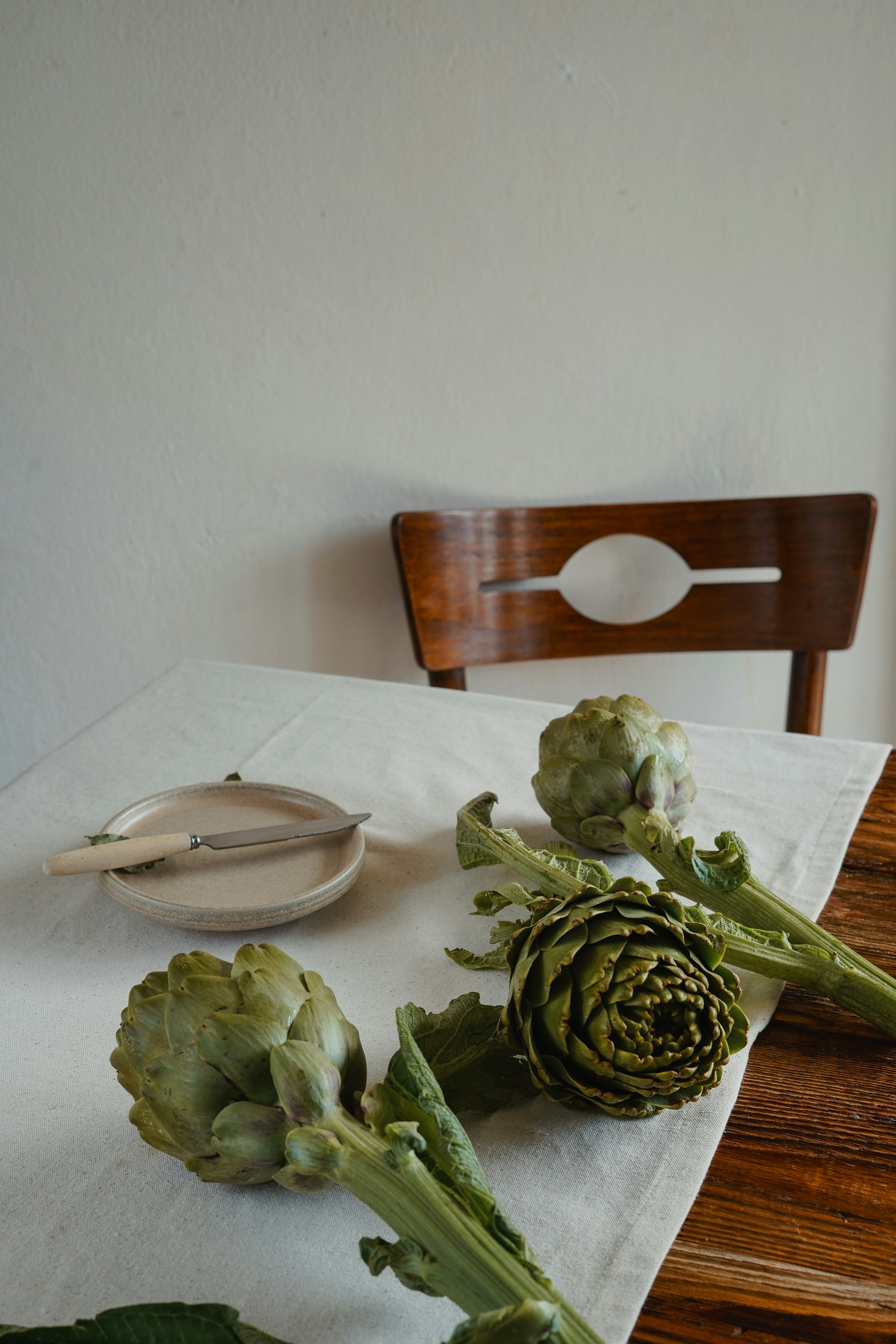 Artischocken, Teller und Stuhl auf einem Tisch.