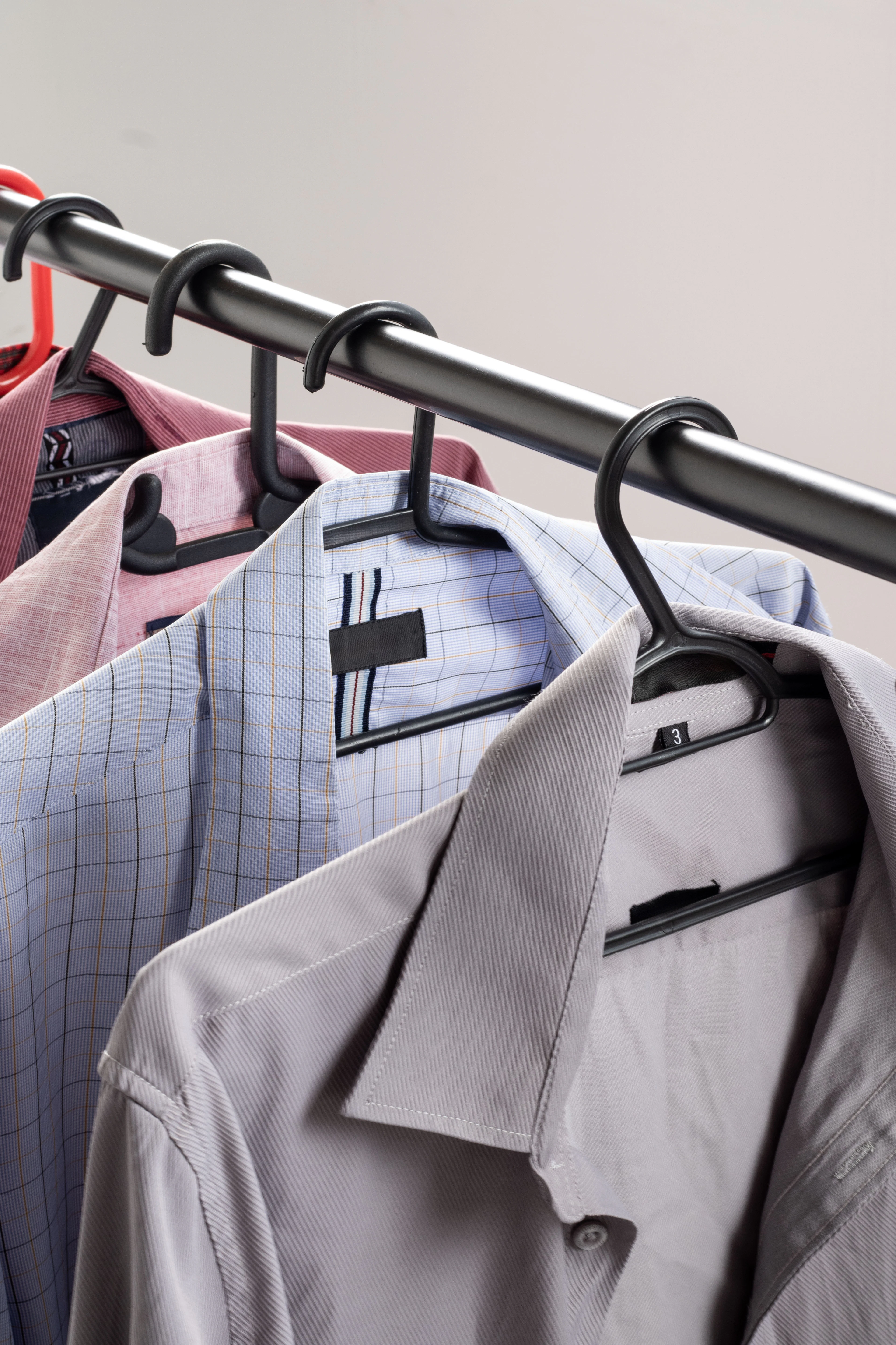 Tailored jackets and shirts in soft neutral tones hanging on a black rail.