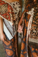 Two people wearing batik fabric hold hands.