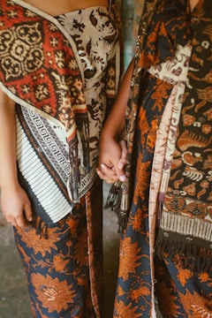 Two people wearing batik fabric hold hands.