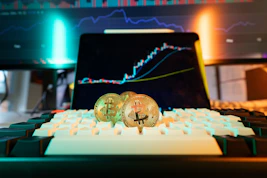 Bitcoin coins rest on a keyboard with stock charts