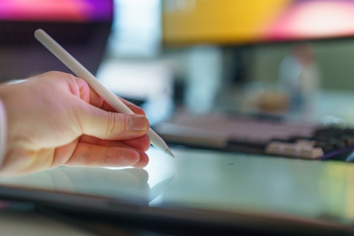 A hand holds a stylus above a tablet.