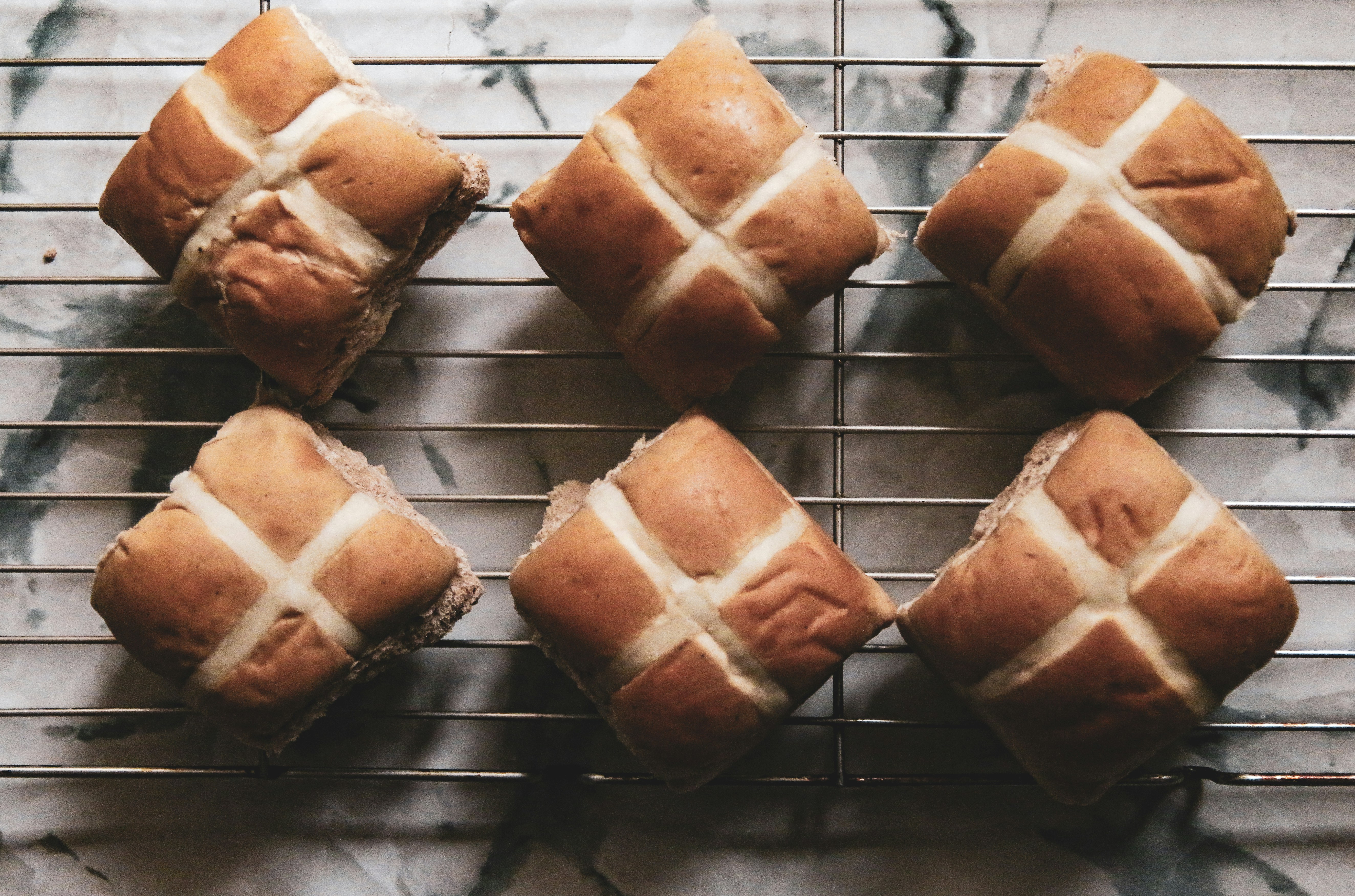 Freshly baked hot cross buns sit on a wire rack.