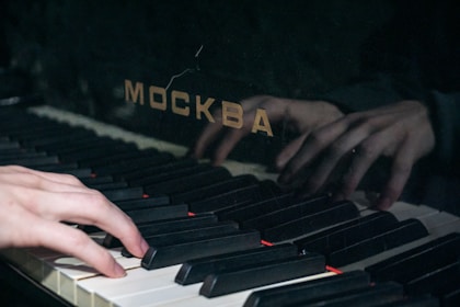 Hands are playing a piano with the name "москва."