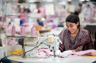 A smiling woman sews at a sewing machine.